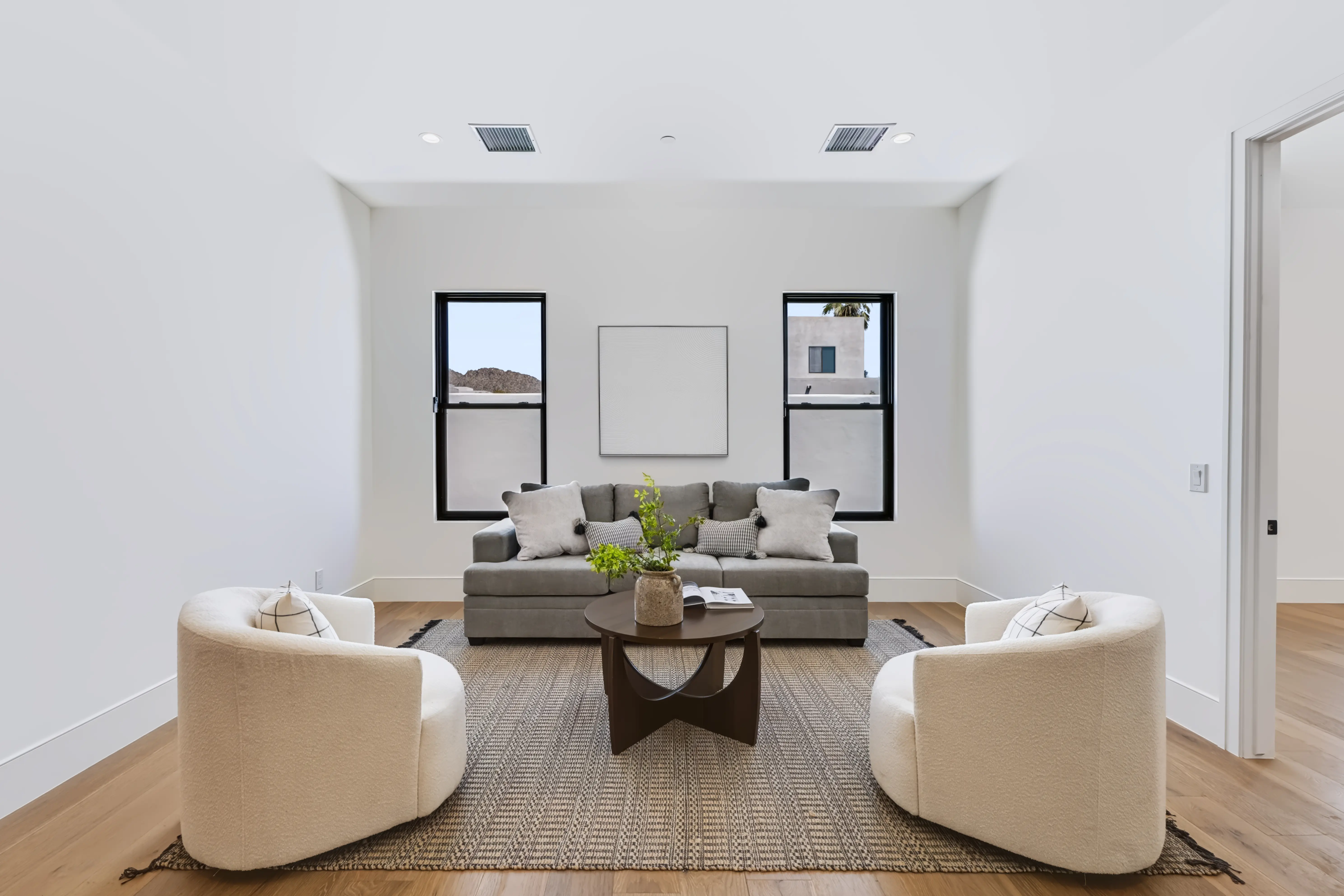 Formal sitting room with symmetrical black-framed windows, a grey sofa and two bouclé swivel chairs