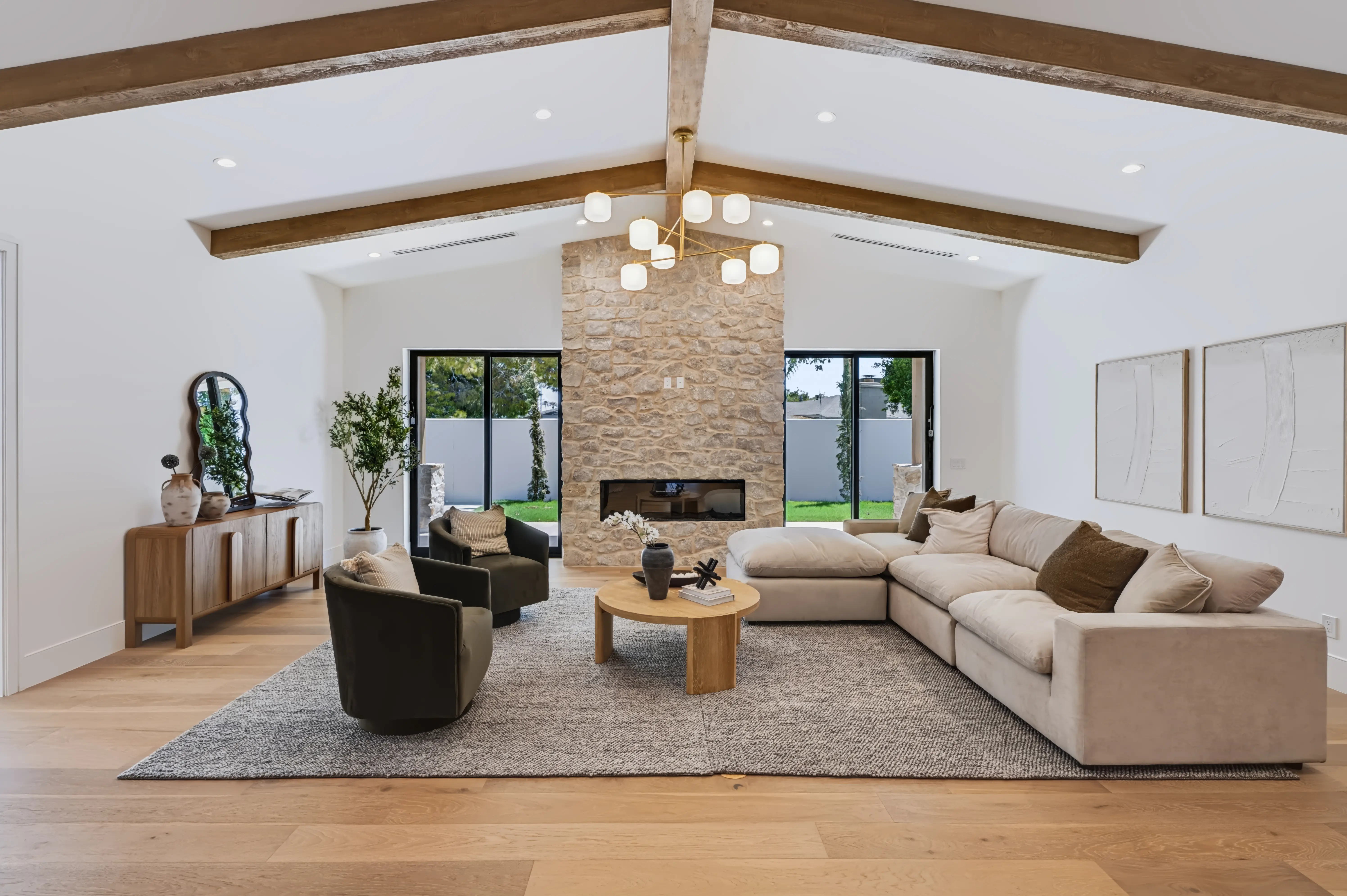 Vaulted great room with a floor-to-ceiling stacked-stone fireplace between two sliding glass walls and exposed white-oak beams