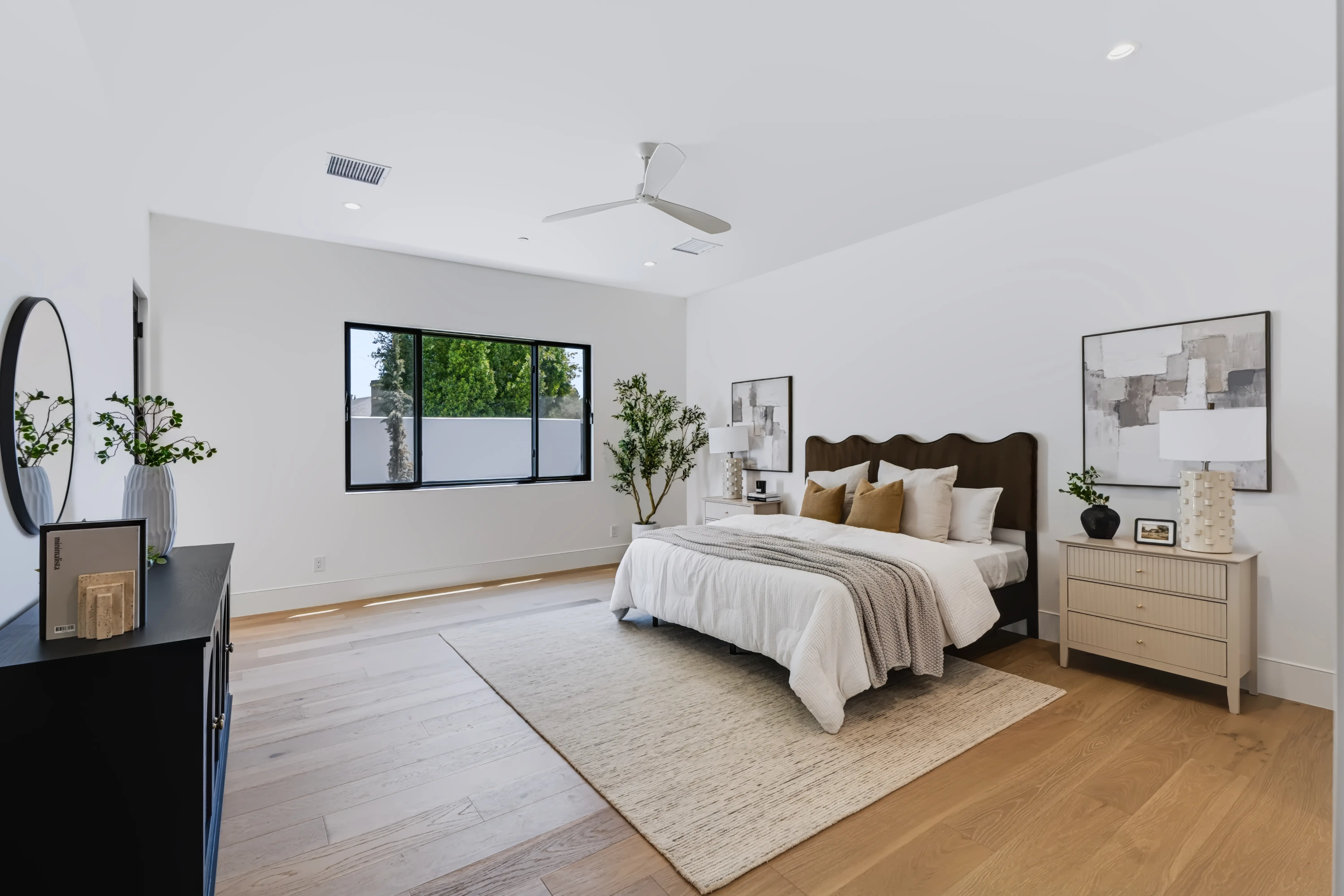 Primary bedroom with a scalloped upholstered headboard, layered neutral bedding and white-oak floors