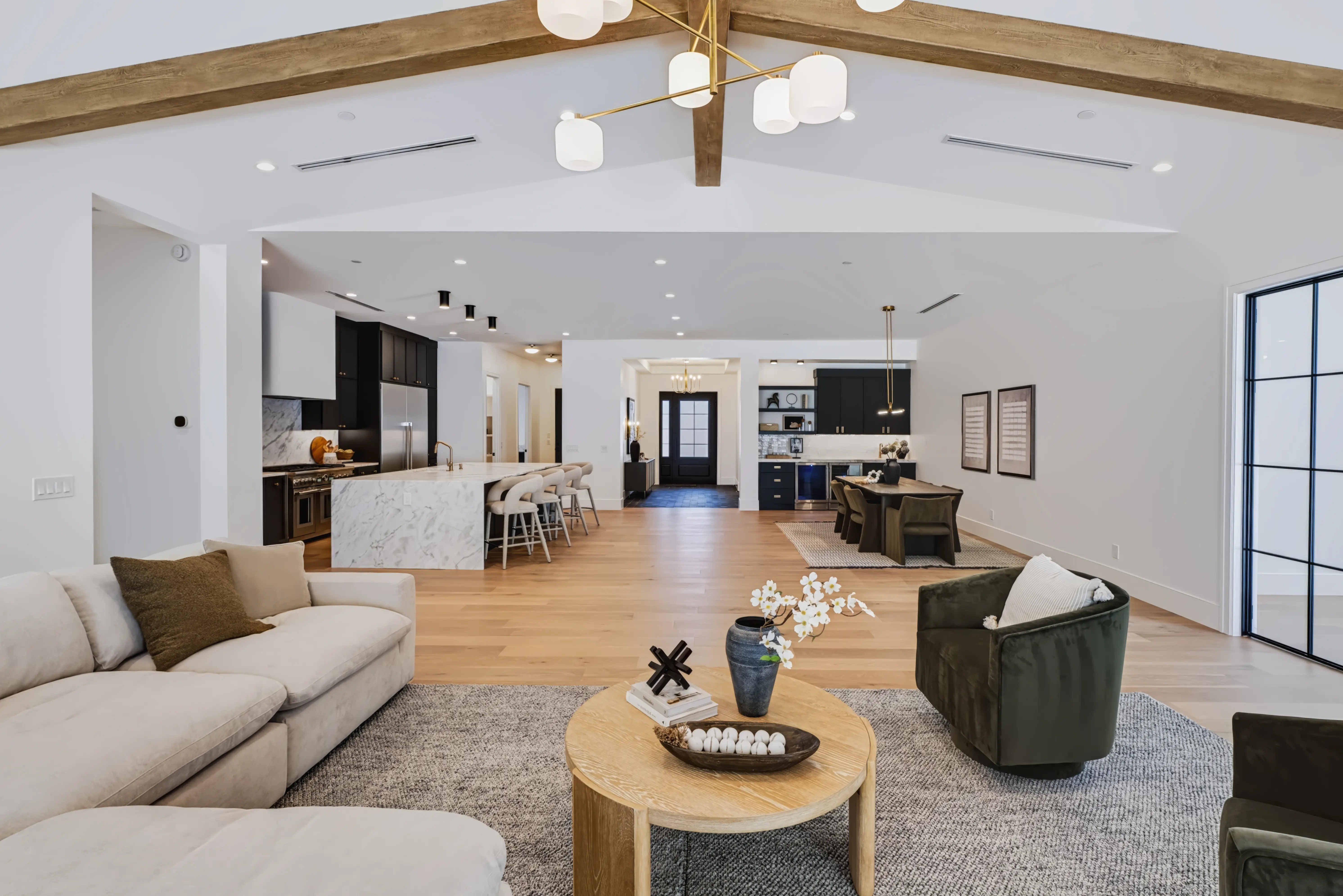 Great room open to the marble island kitchen and dining beyond, under a beamed cathedral ceiling