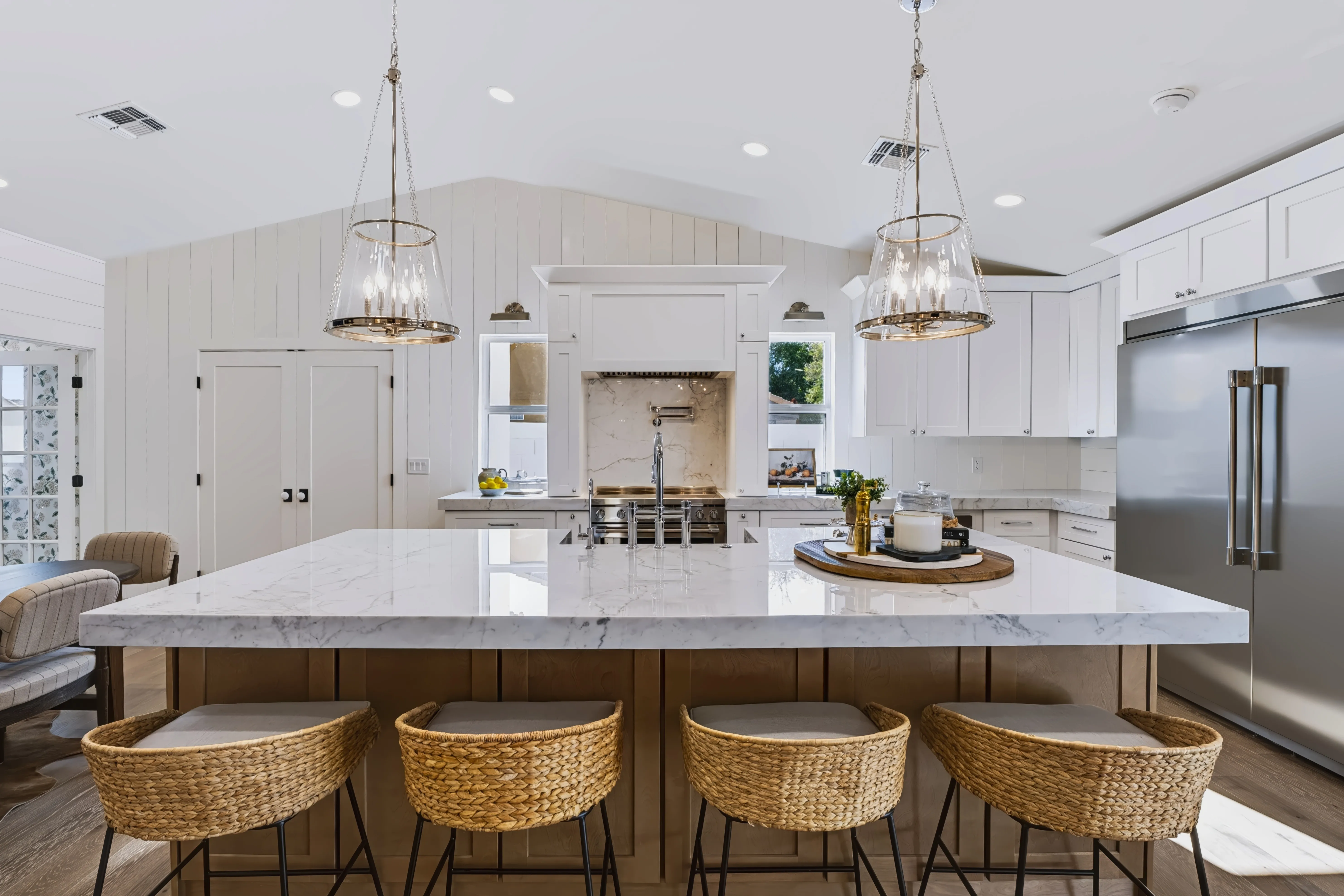 Farmhouse kitchen with an oversized marble island, woven counter stools and a vaulted shiplap ceiling