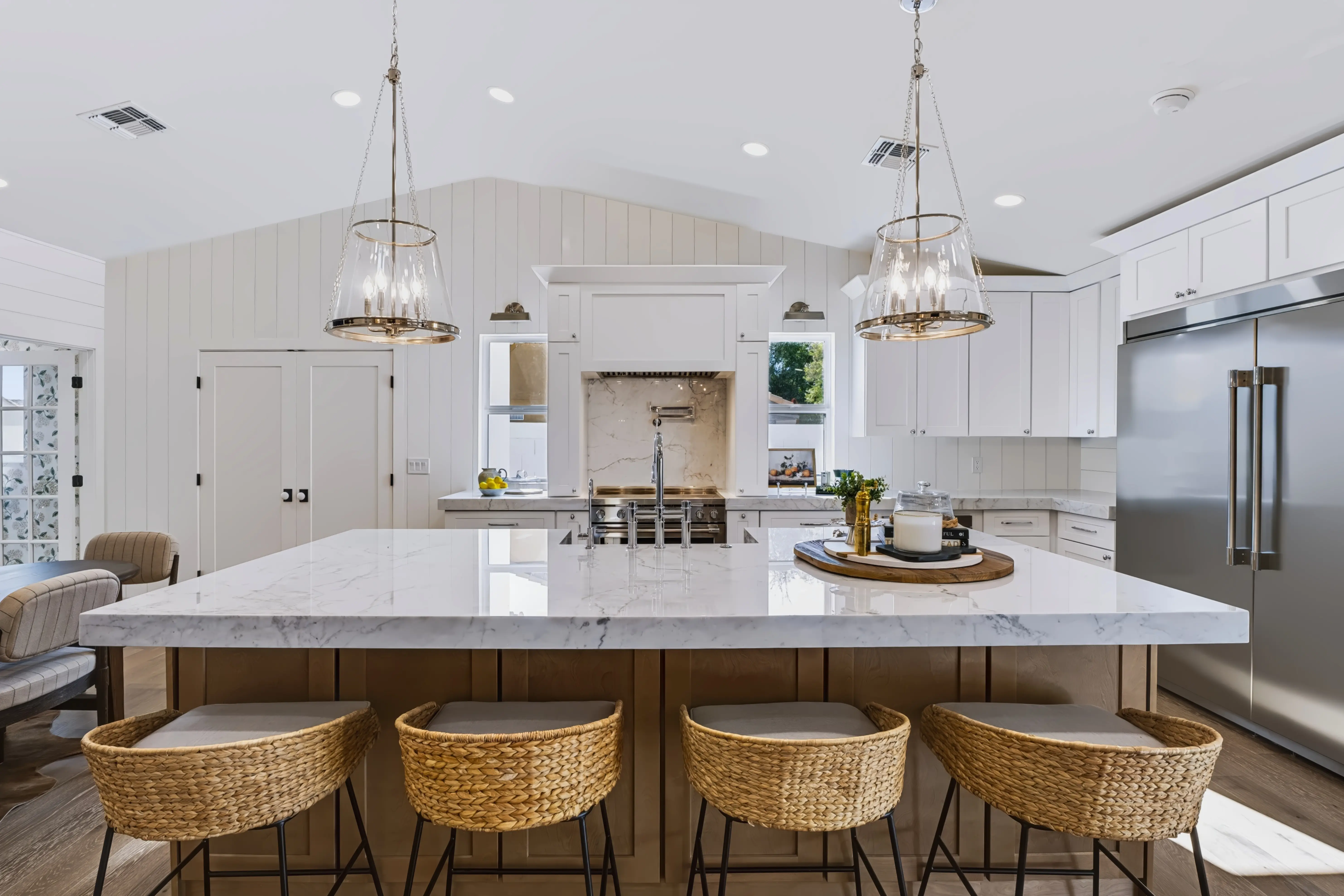 Farmhouse kitchen with an oversized marble island, woven counter stools and a vaulted shiplap ceiling