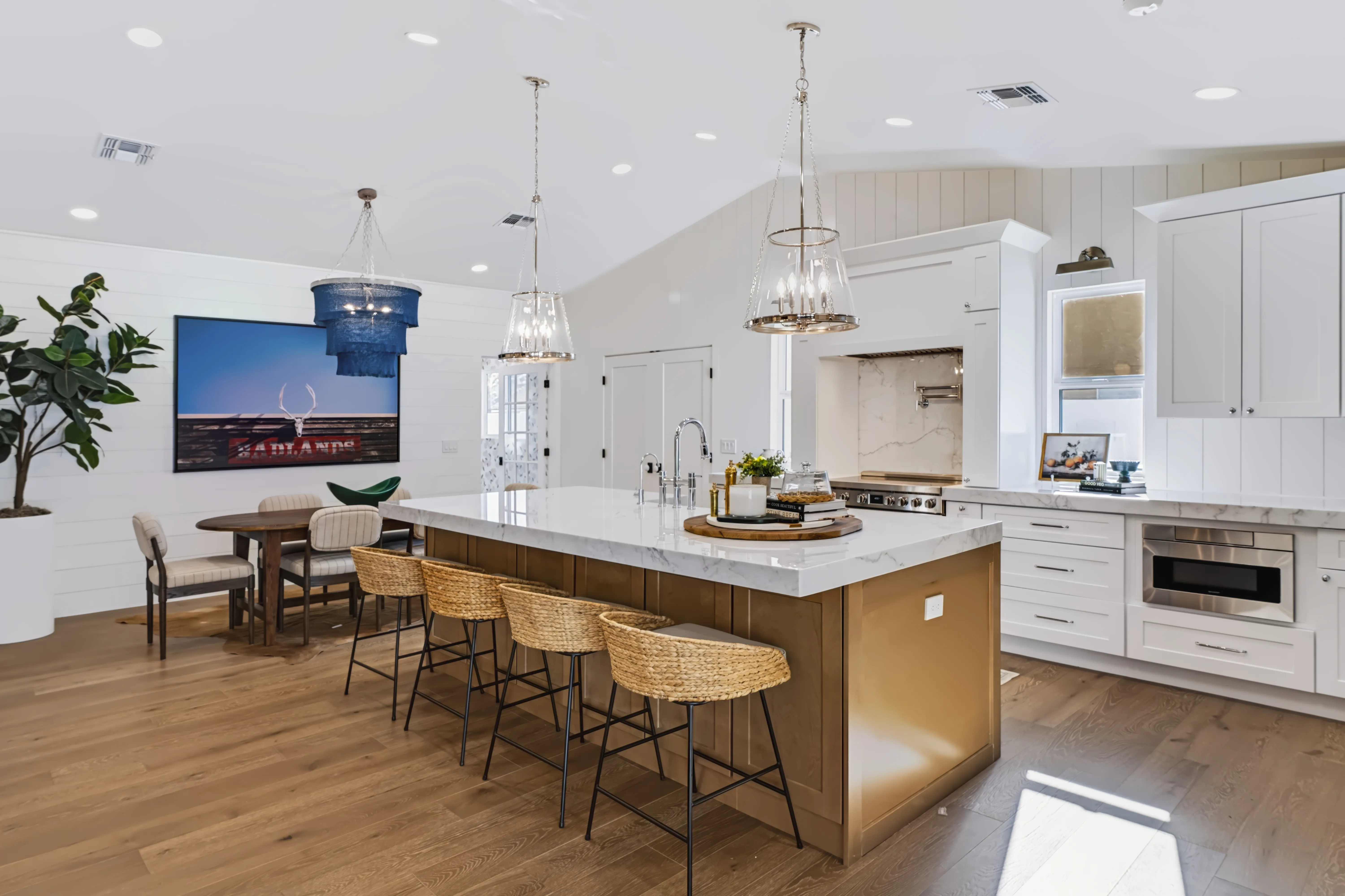 A vaulted kitchen and dining area with a marble island, woven counter stools and a shiplap ceiling