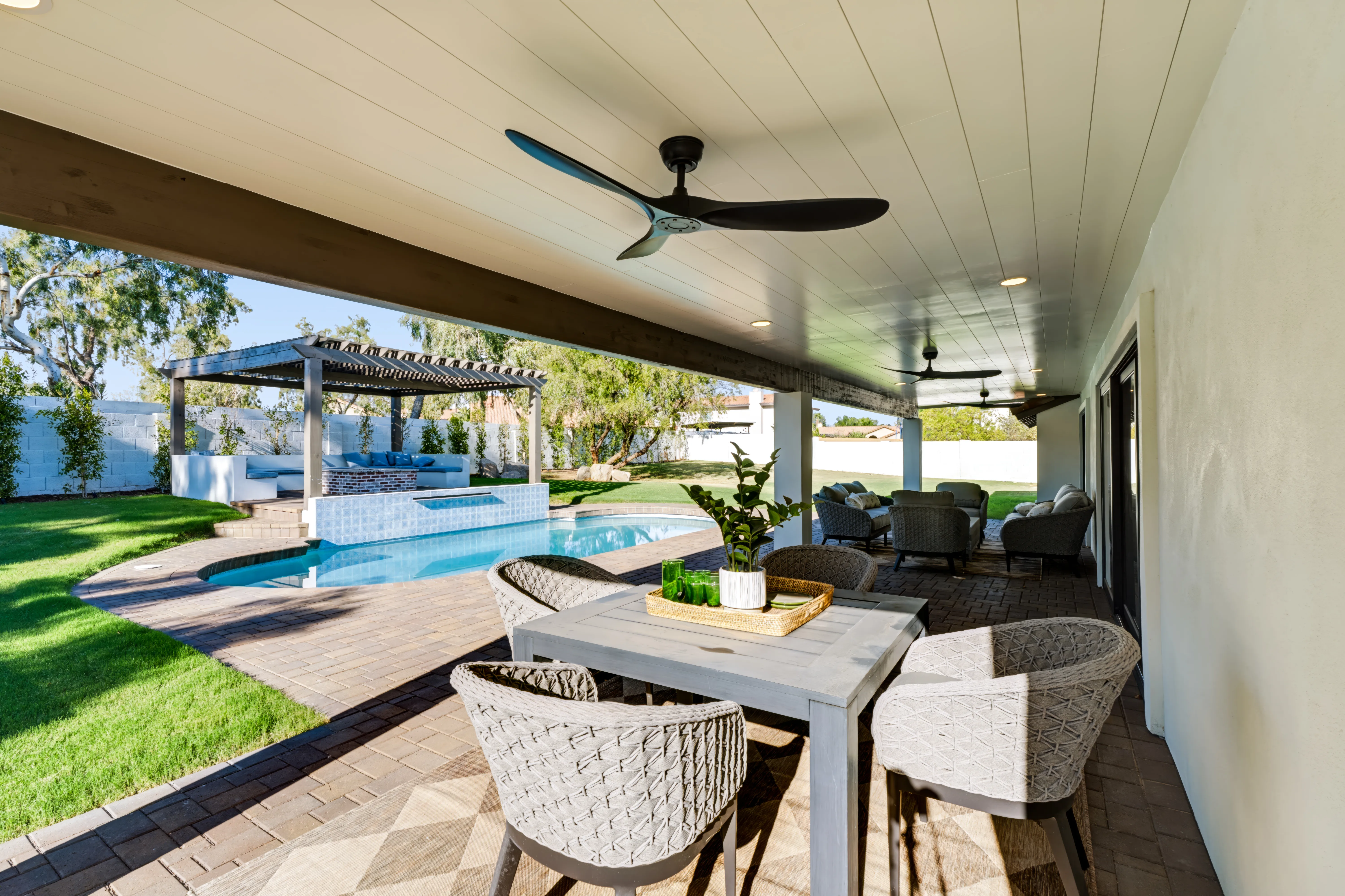Covered patio with a paddle fan looking out to the pool, a pergola lounge and cushioned seating