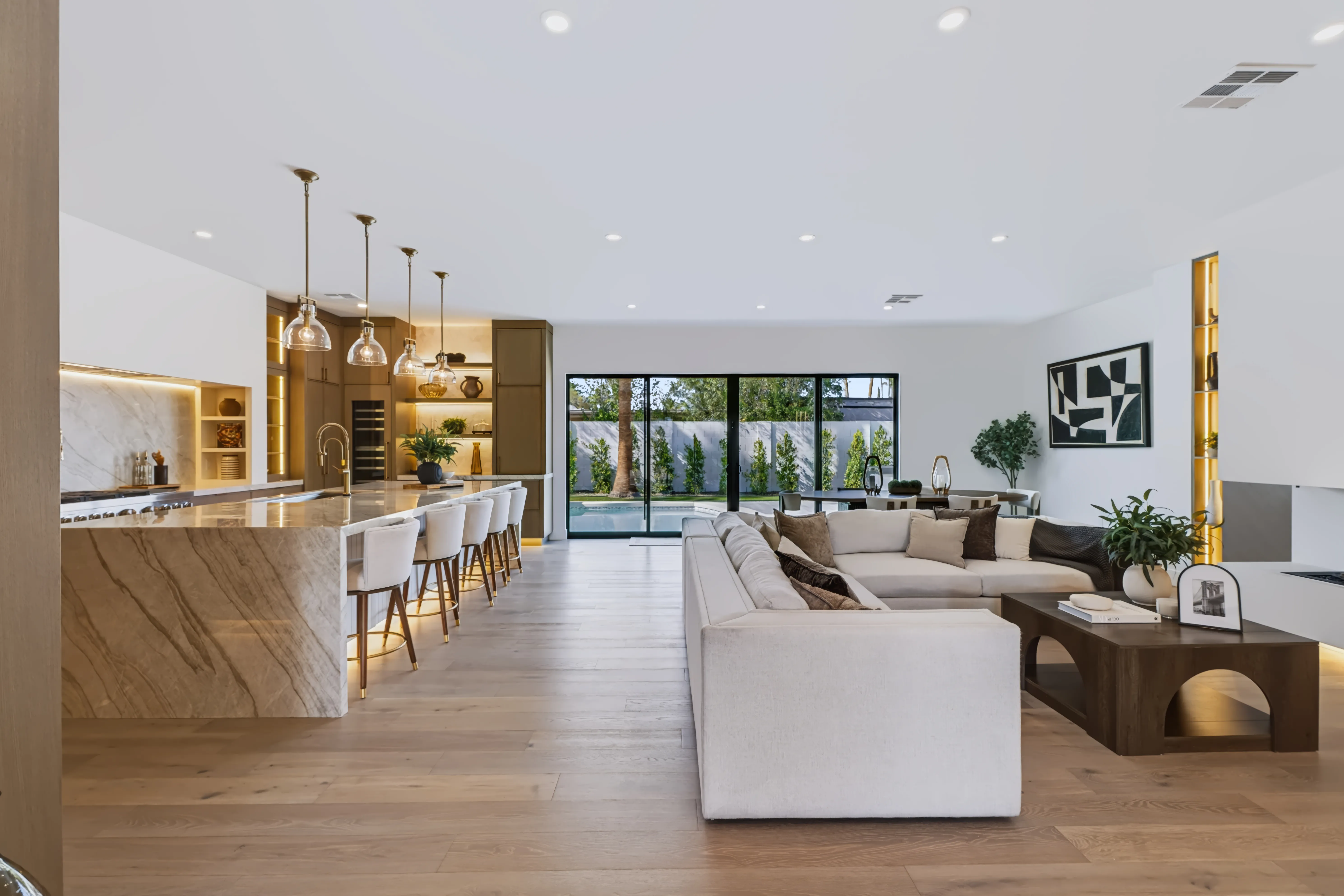 An open-plan great room looking through to a marble island kitchen and a wall of glass onto the pool