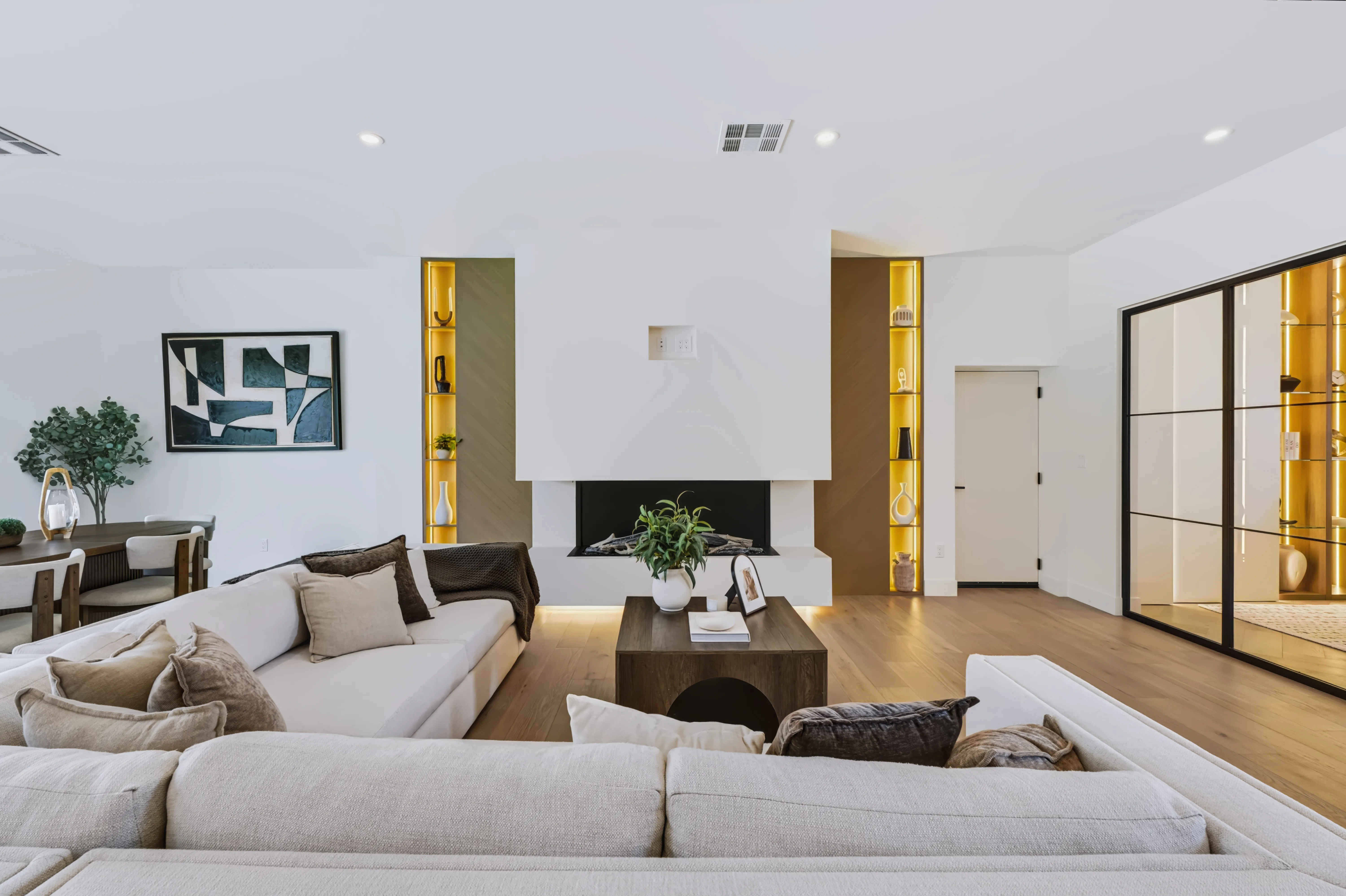 Living area with a raised linear fireplace flanked by brass-lit display niches and a low sectional