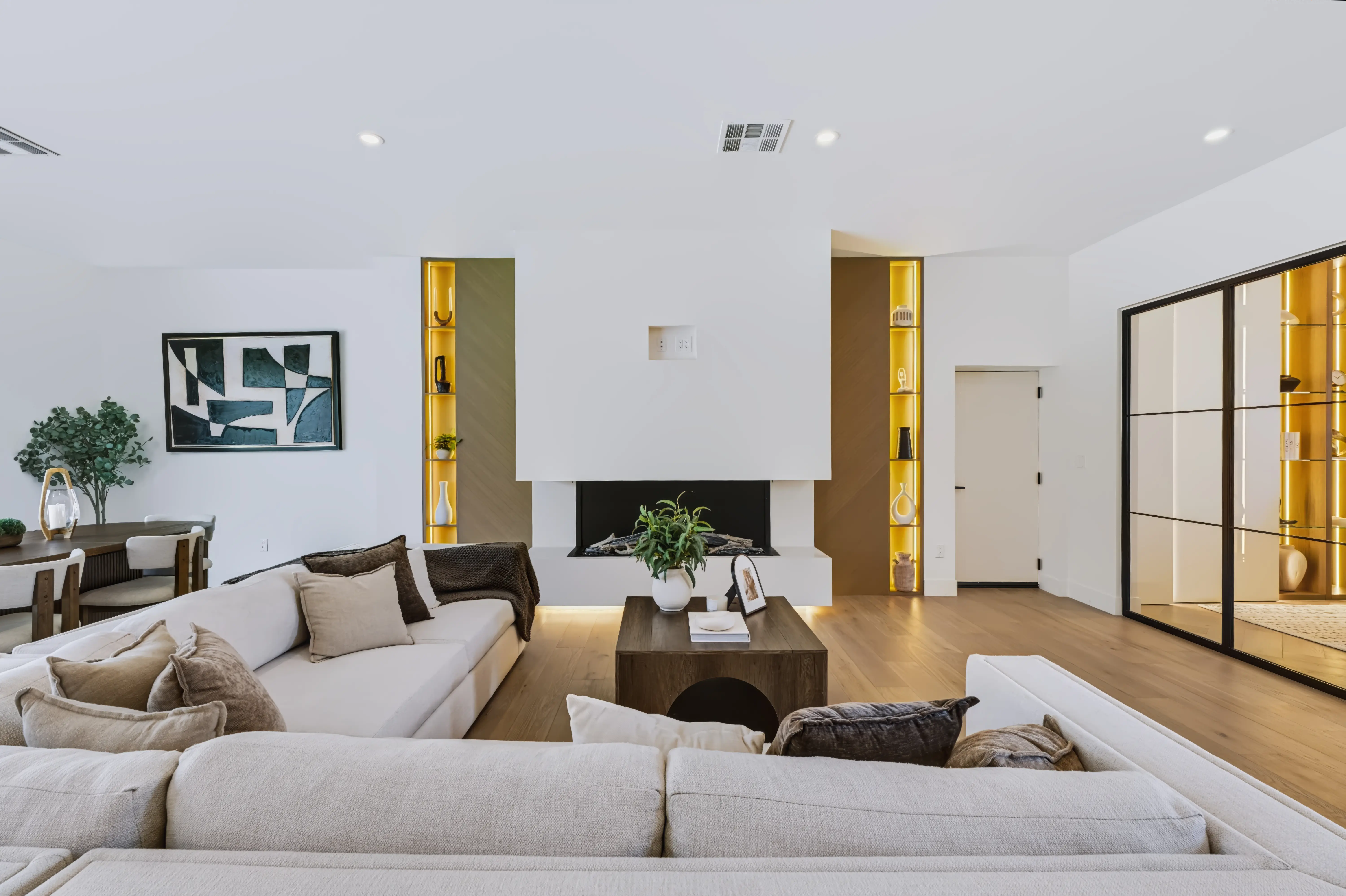 Living area with a raised linear fireplace flanked by brass-lit display niches and a low sectional