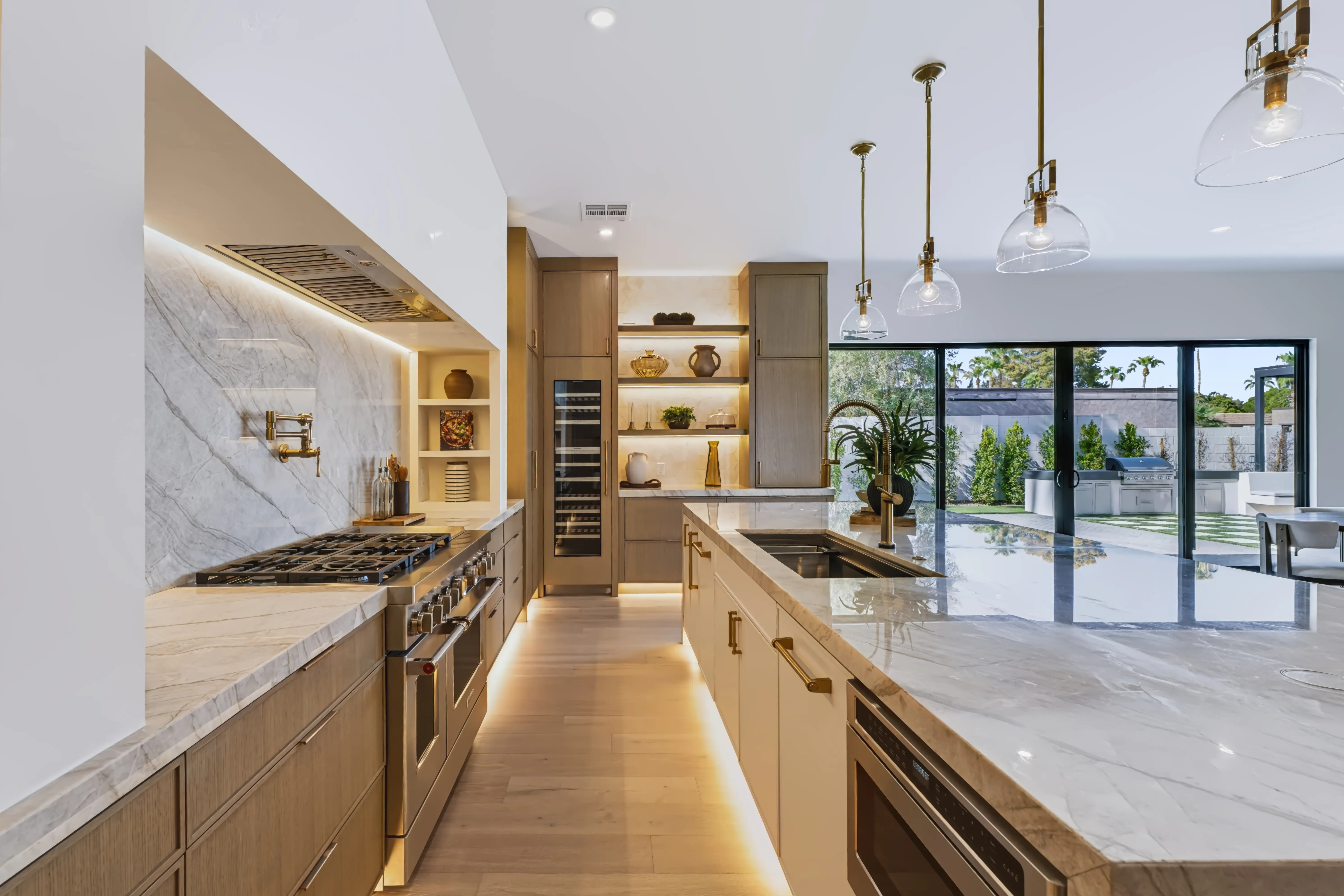 Chef's run with a stainless range and pot filler, the island beyond framing the covered patio and outdoor kitchen