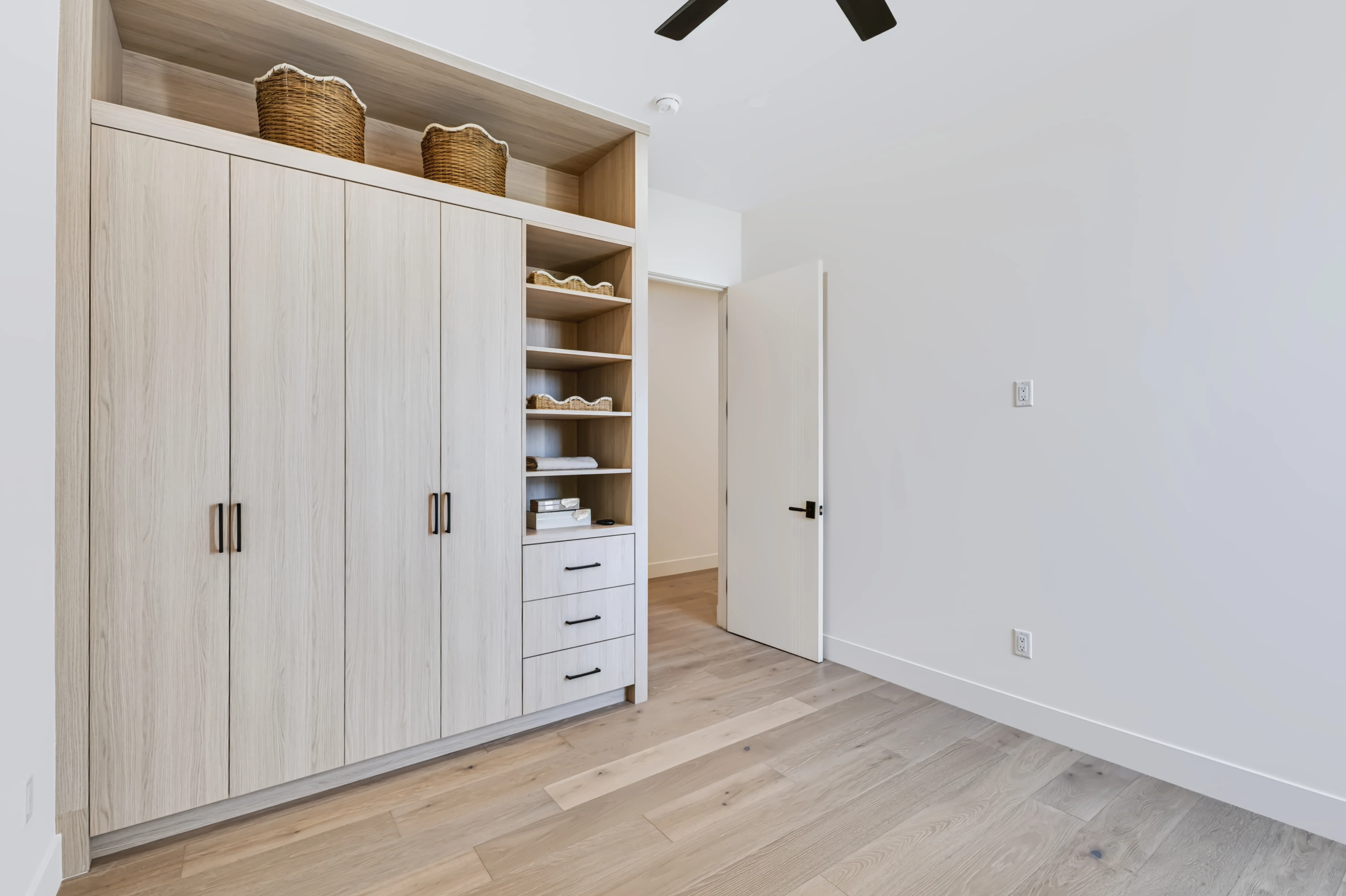 Secondary bedroom with a built-in light oak wardrobe wall and open shelving beside the hall door
