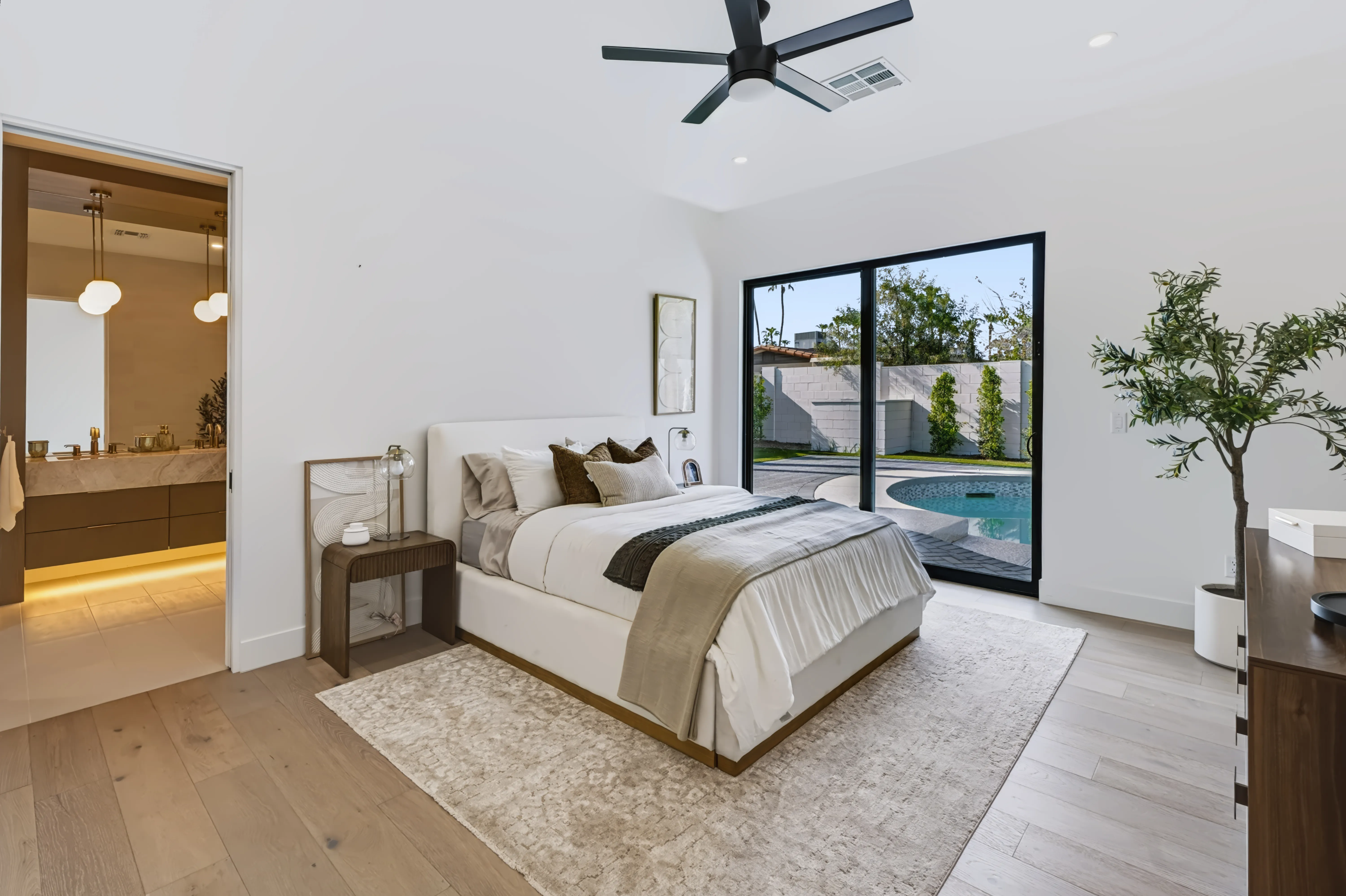 Primary bedroom with an upholstered bed, sliding glass to the pool, and the ensuite bath visible through a pocket door
