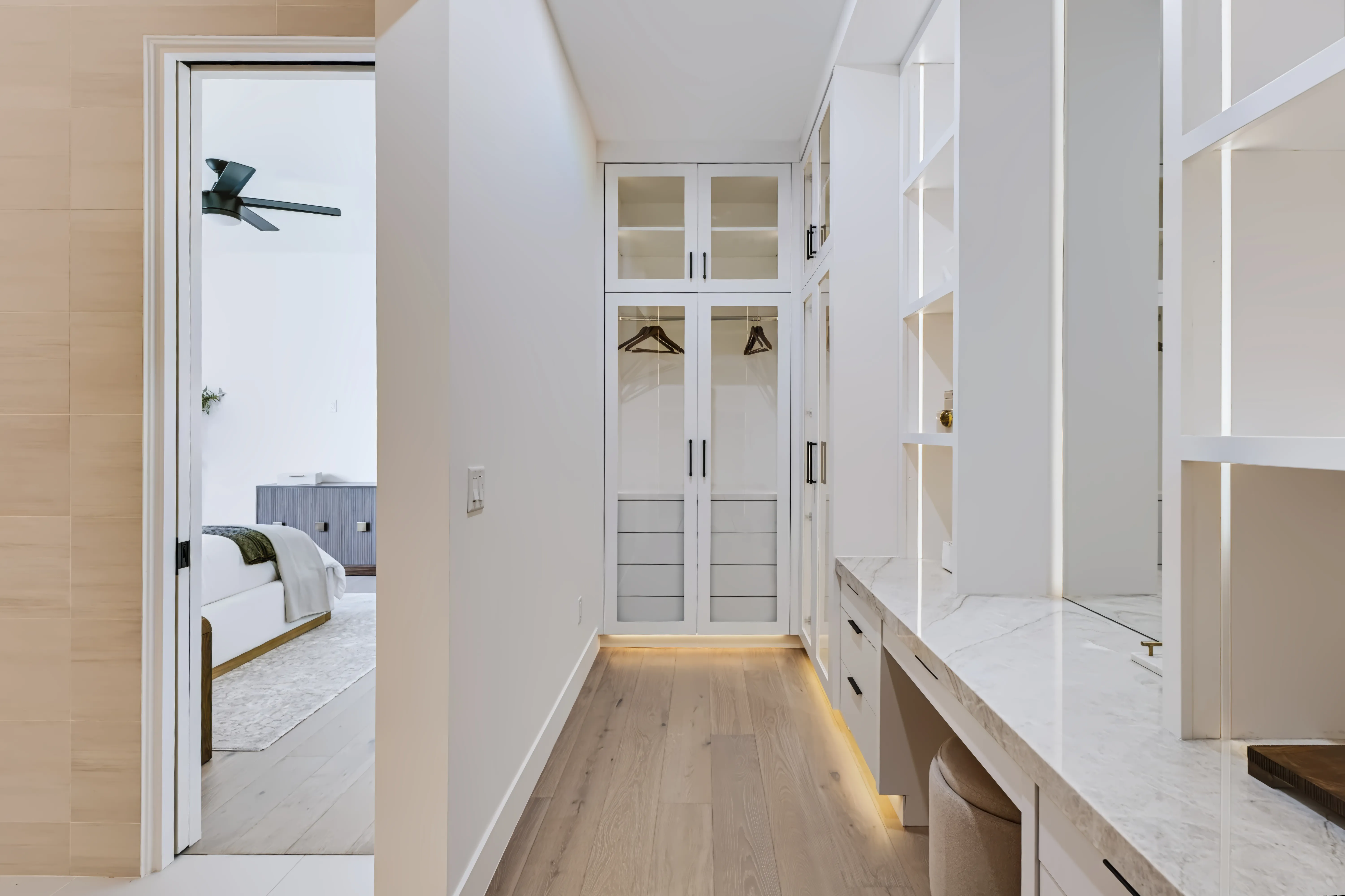 Walk-through dressing room with glass-front wardrobes, a marble vanity counter, and light oak floors