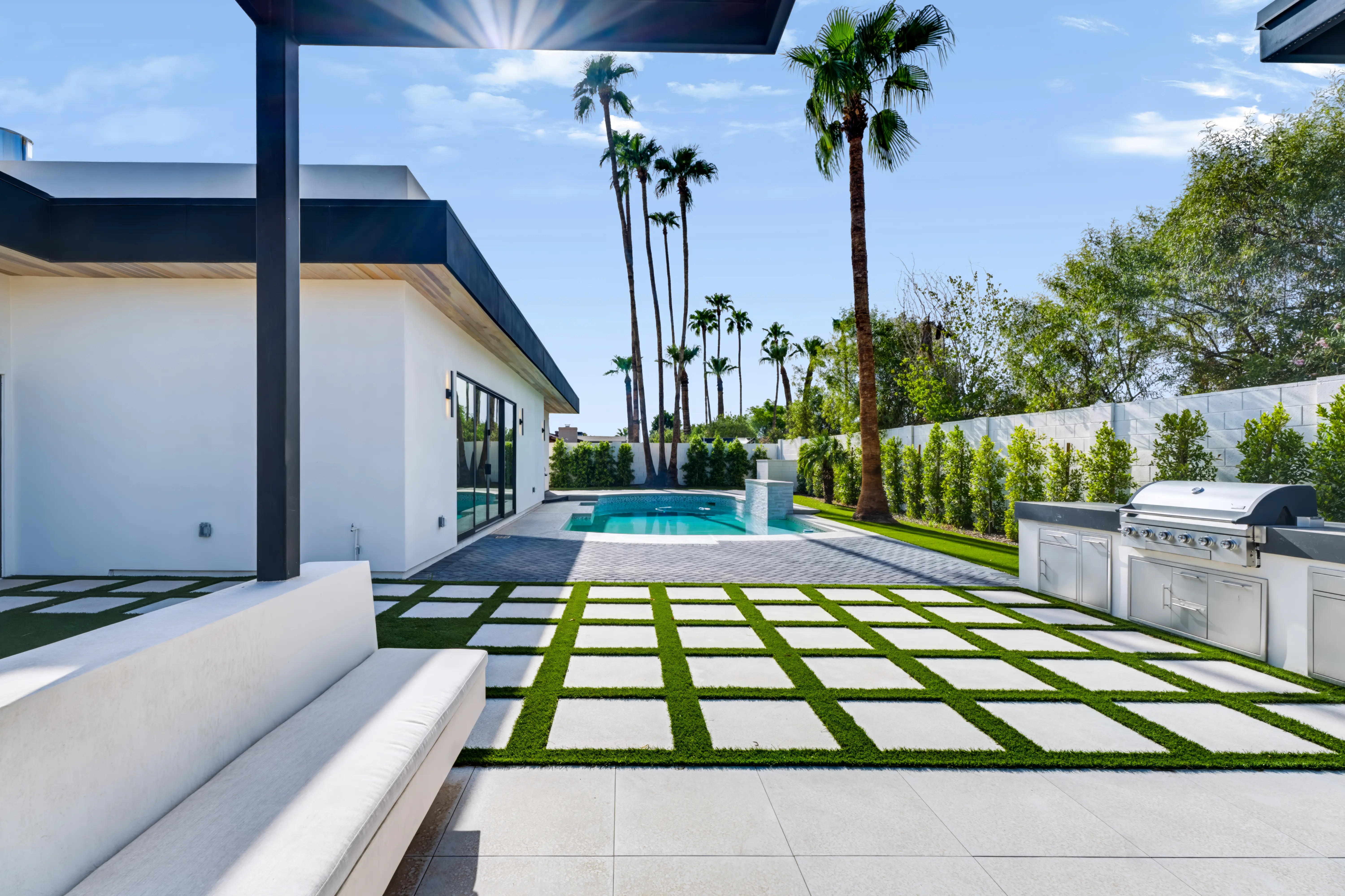 Backyard from the covered patio, turf-inlaid pavers leading to a freeform pool with mature palms along the wall