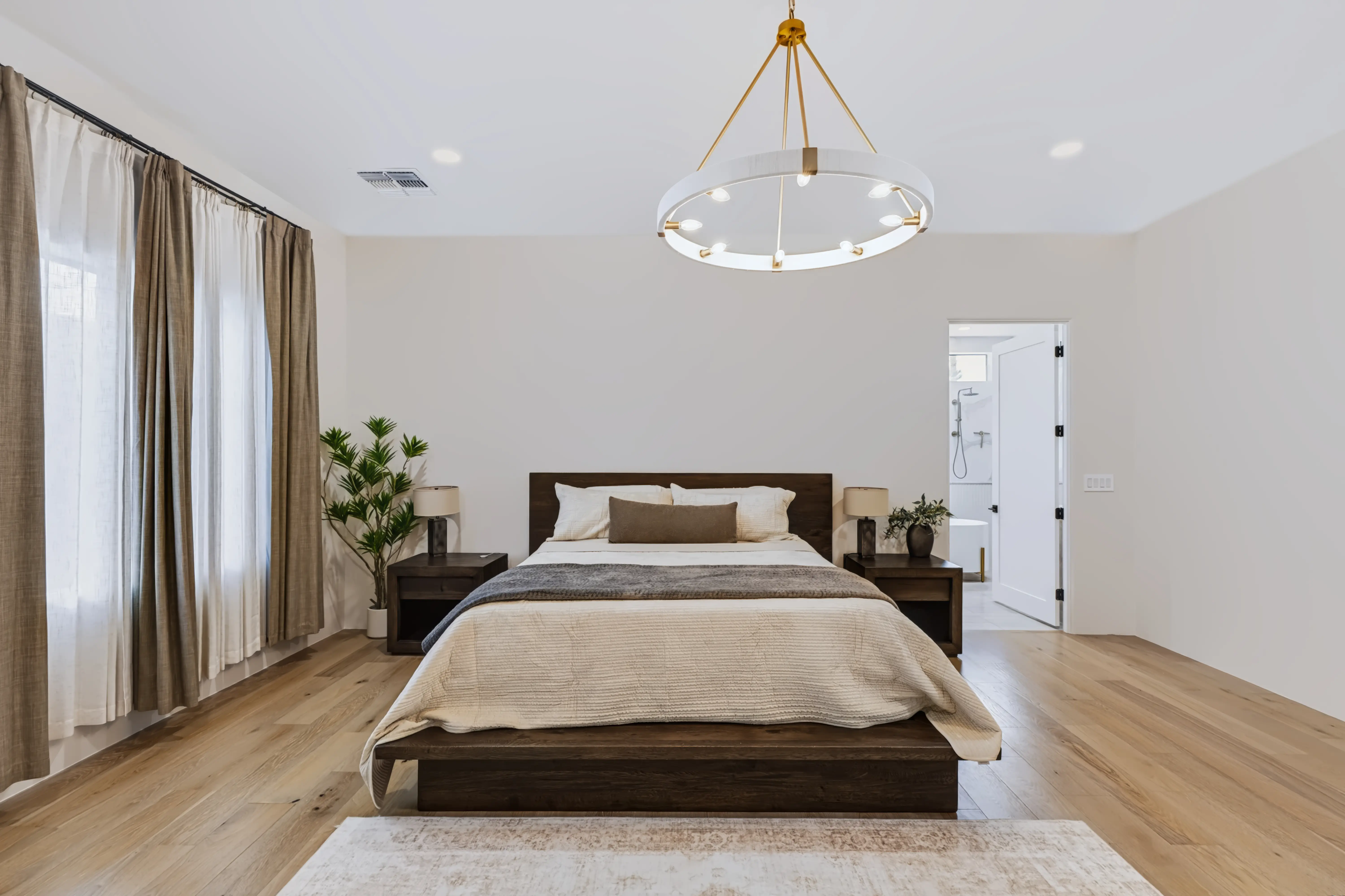 Primary bedroom with a dark wood platform bed, linen drapery and a lit ring chandelier