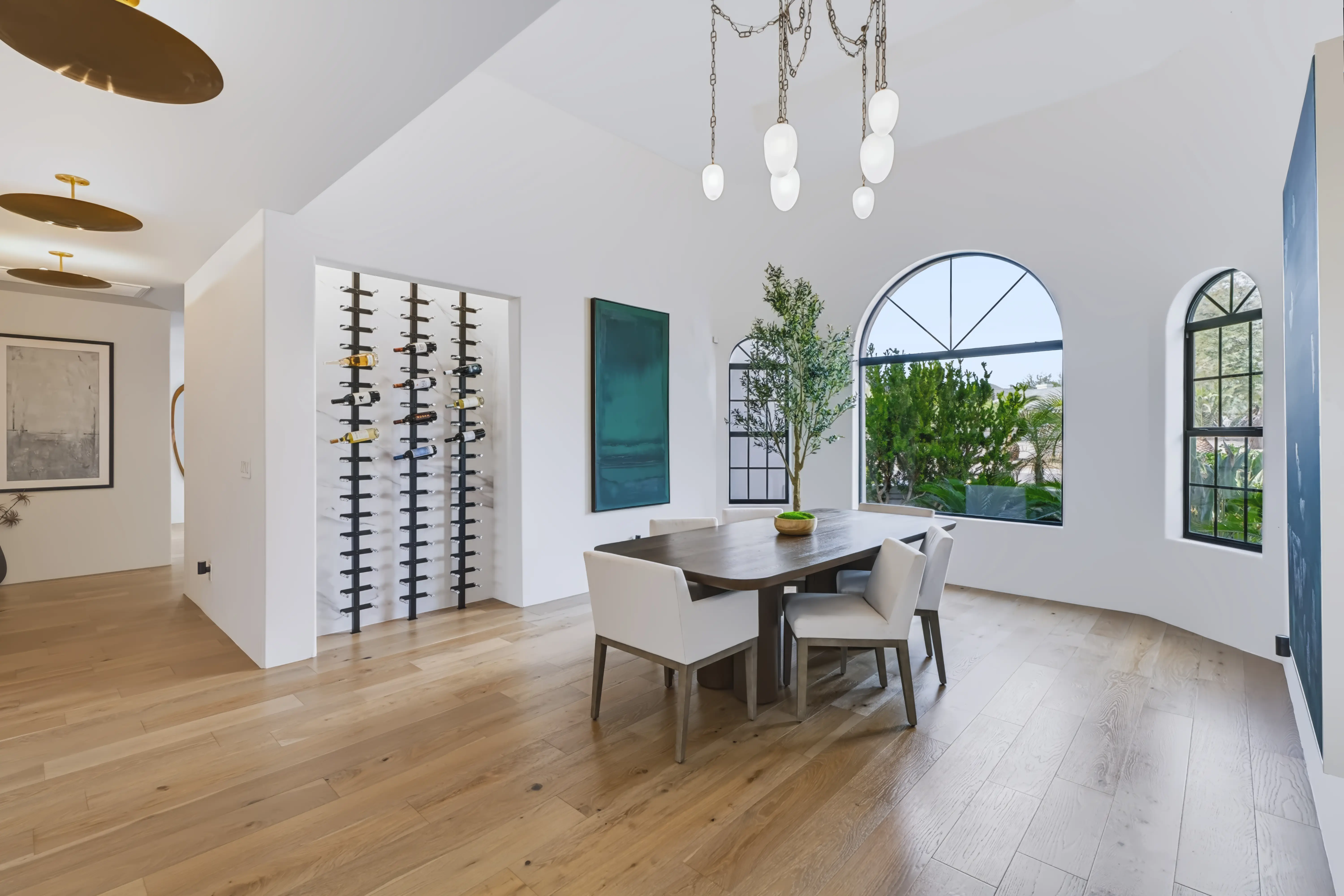 Dining room with a wall-mounted wine display, a dark oak table and a tall arched steel window onto the garden