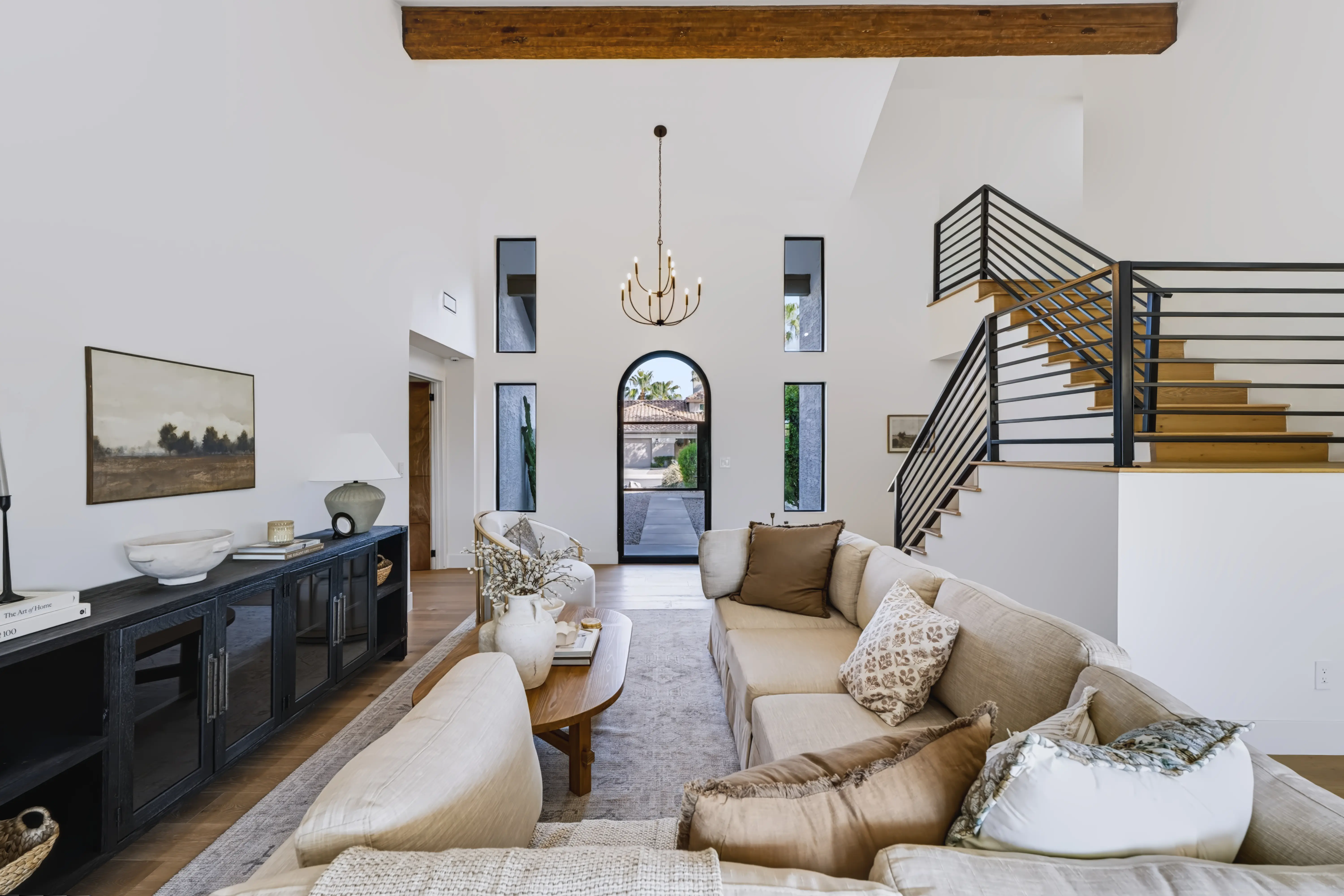 Two-story living room with an arched glass entry door at the far end and a black steel-and-oak staircase