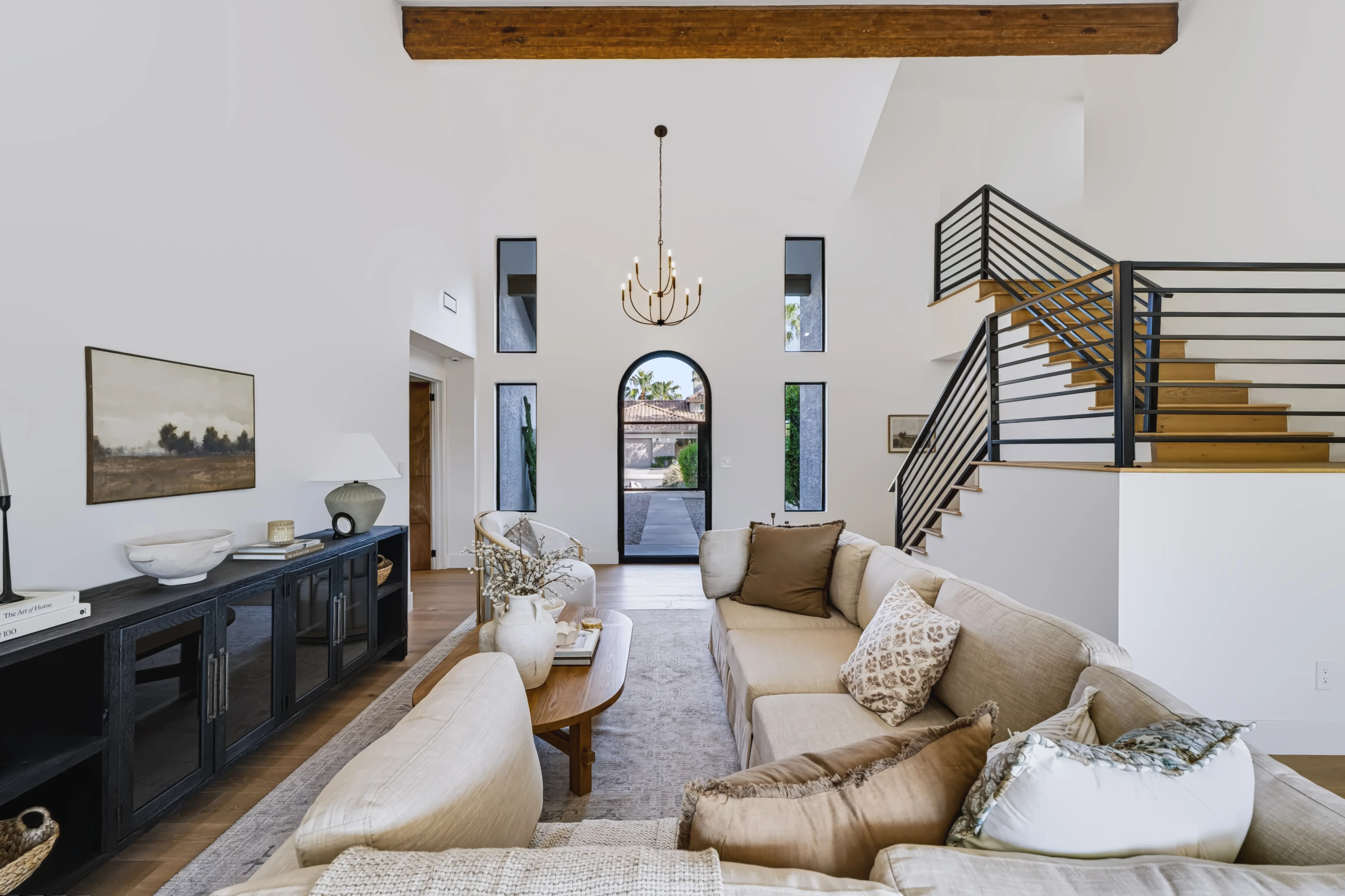 Two-story living room with an arched glass entry door at the far end and a black steel-and-oak staircase