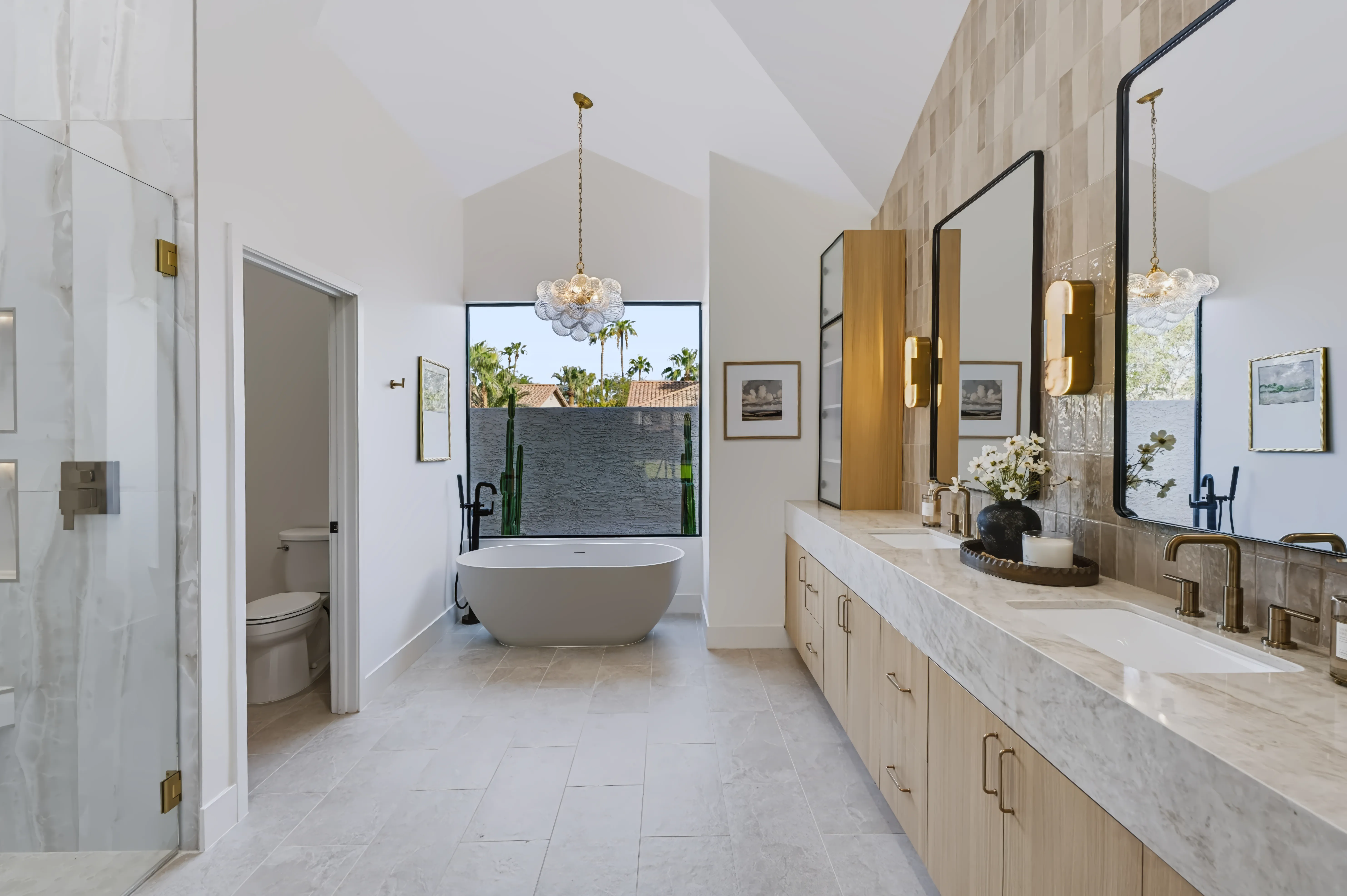Primary bath with a freestanding tub beneath a vaulted window and a long marble double vanity