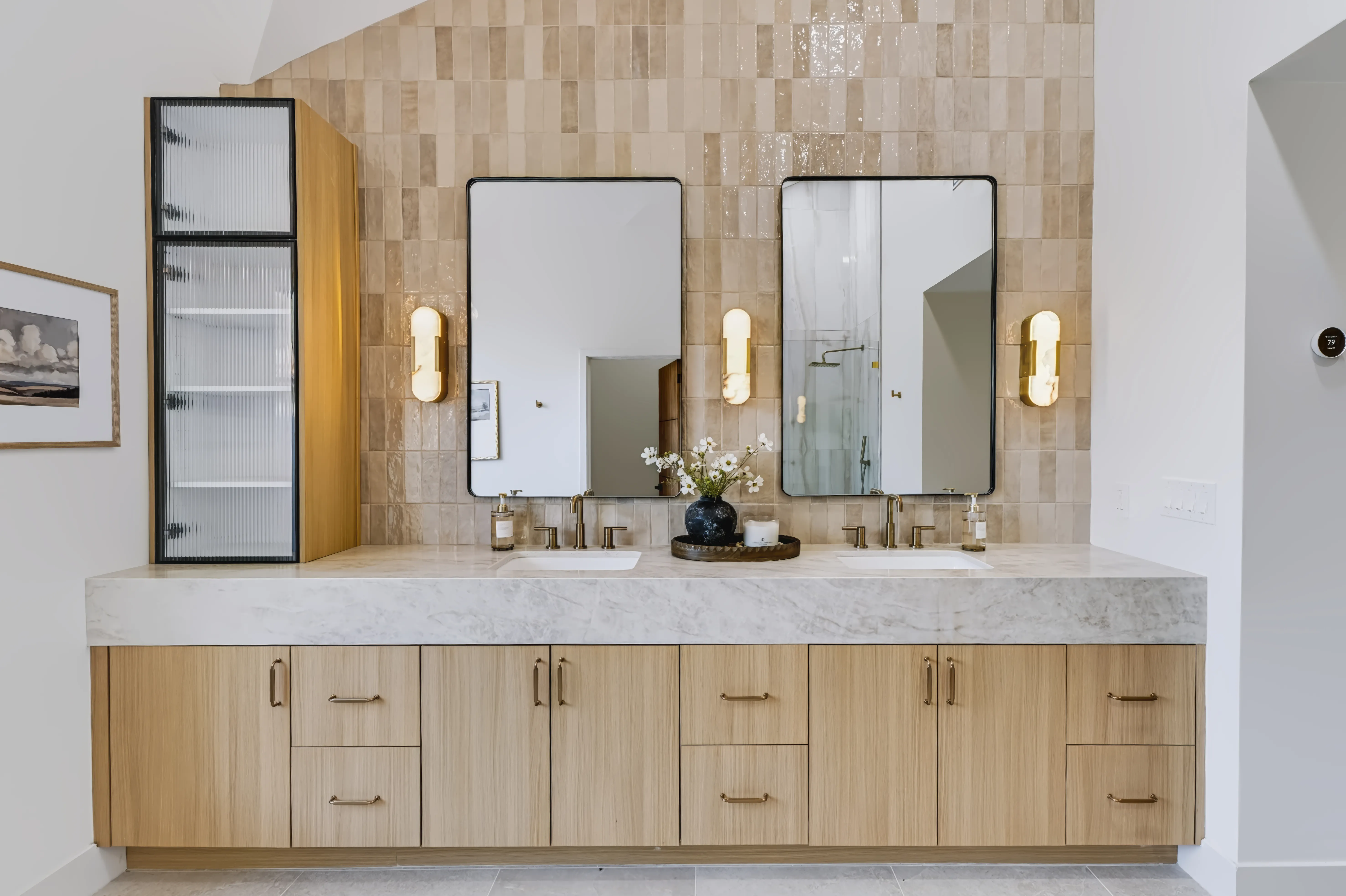 A primary bathroom with a freestanding tub beneath a vaulted window and a long marble double vanity