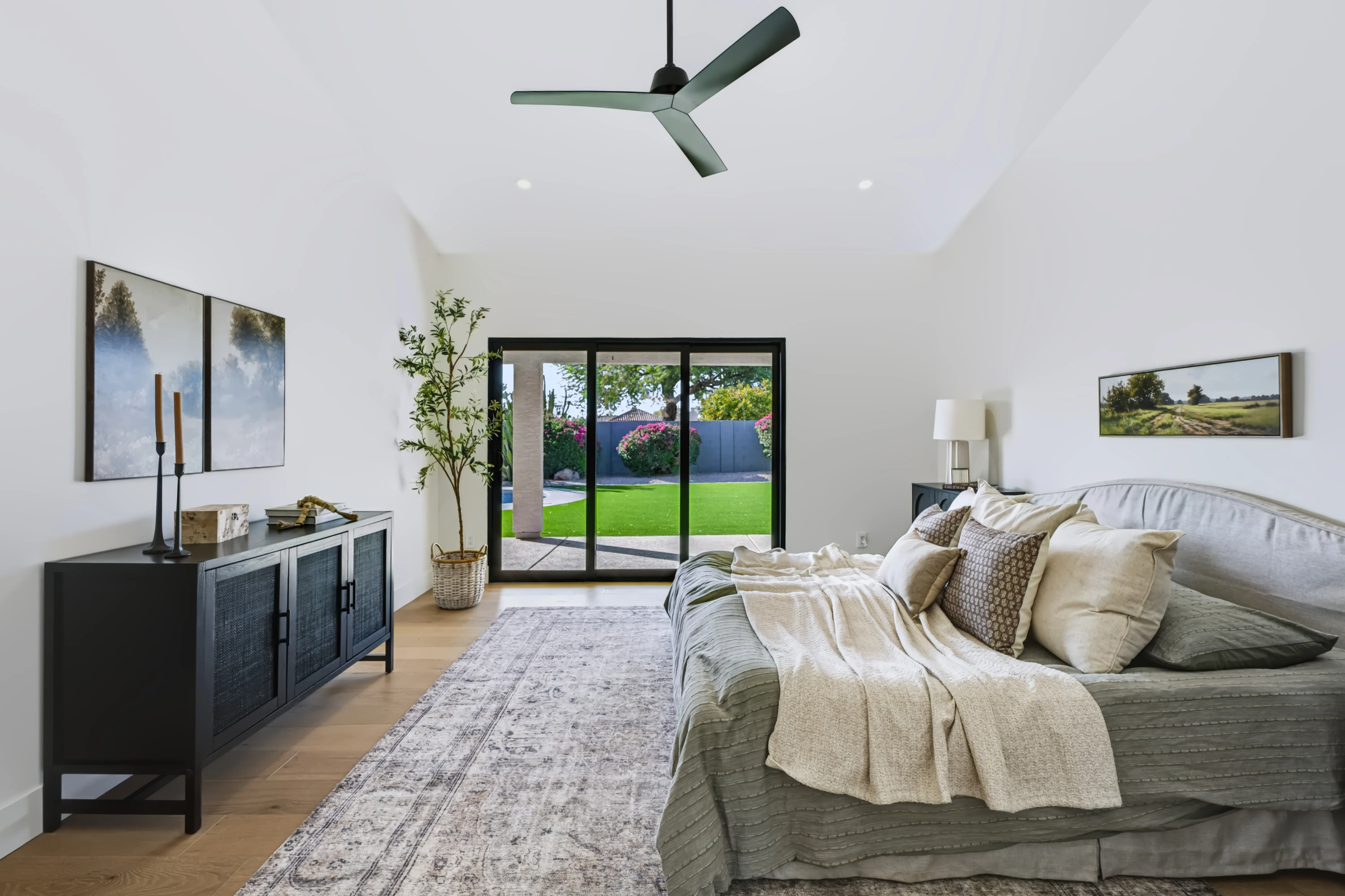 A primary bedroom with a sloped ceiling and sliding glass doors open to a turf lawn and pool
