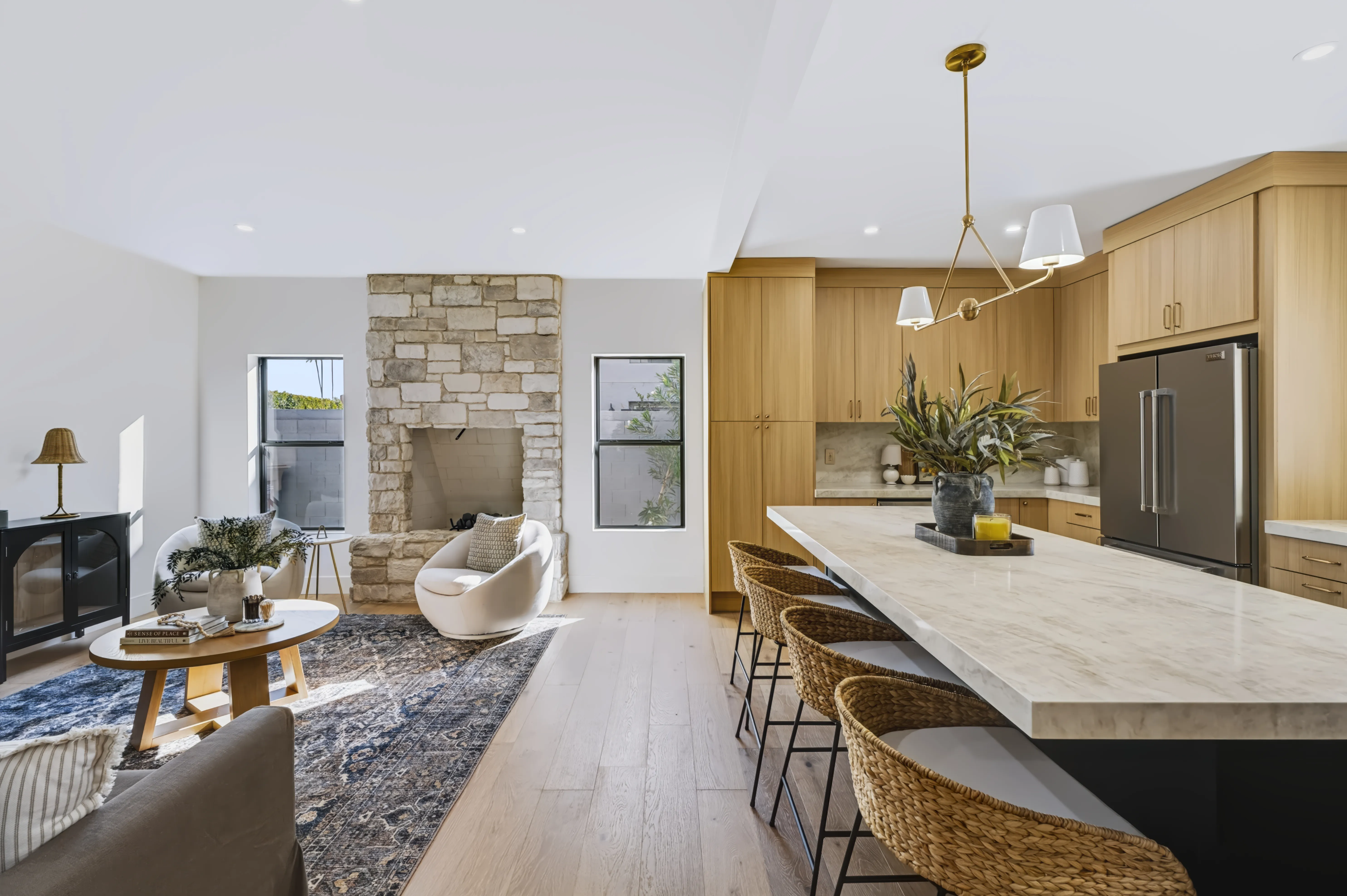 An open living area with a stone fireplace beside a kitchen with a long marble island