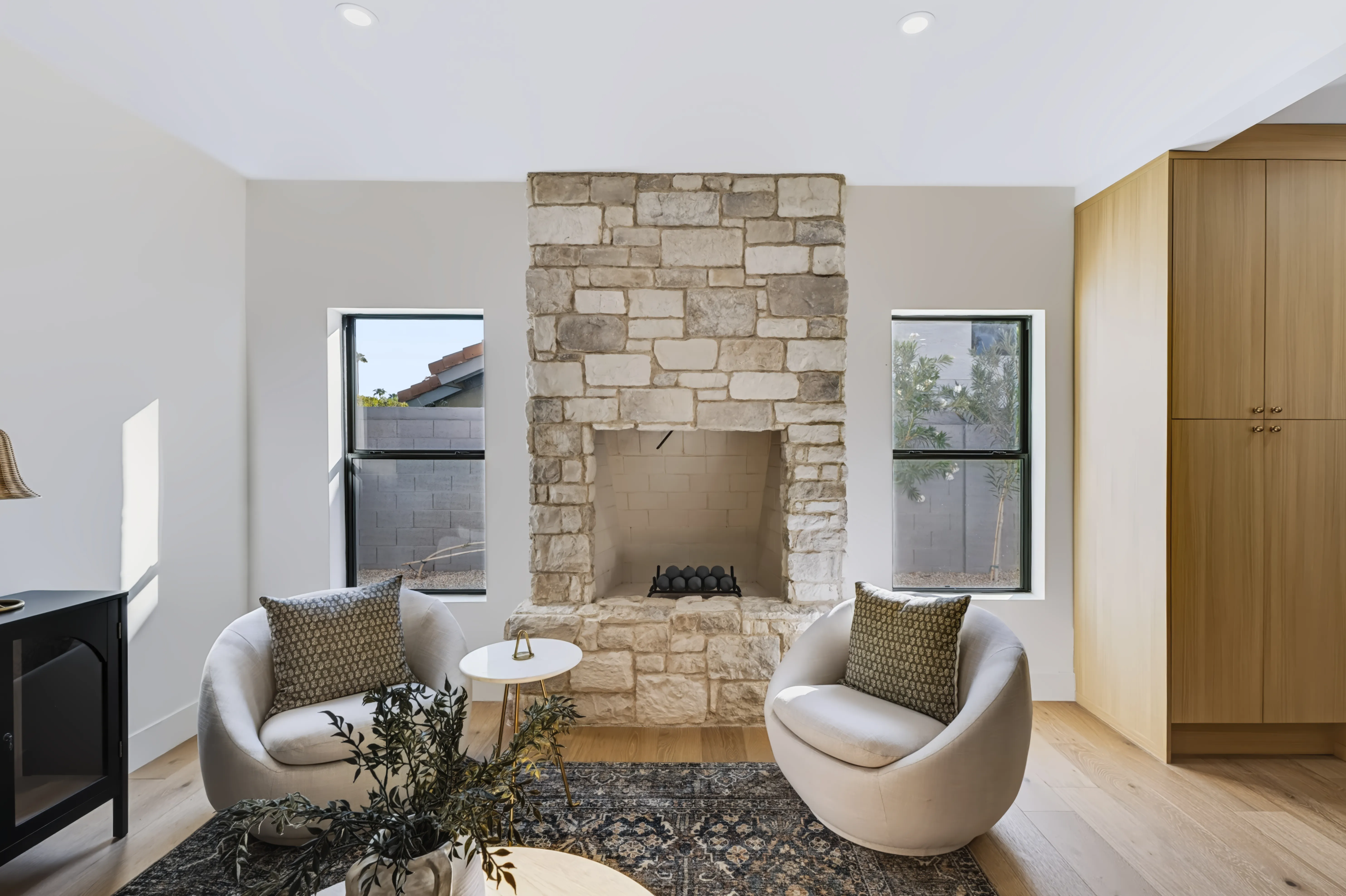 Sitting room built around a stacked-stone fireplace centered between two black-framed windows