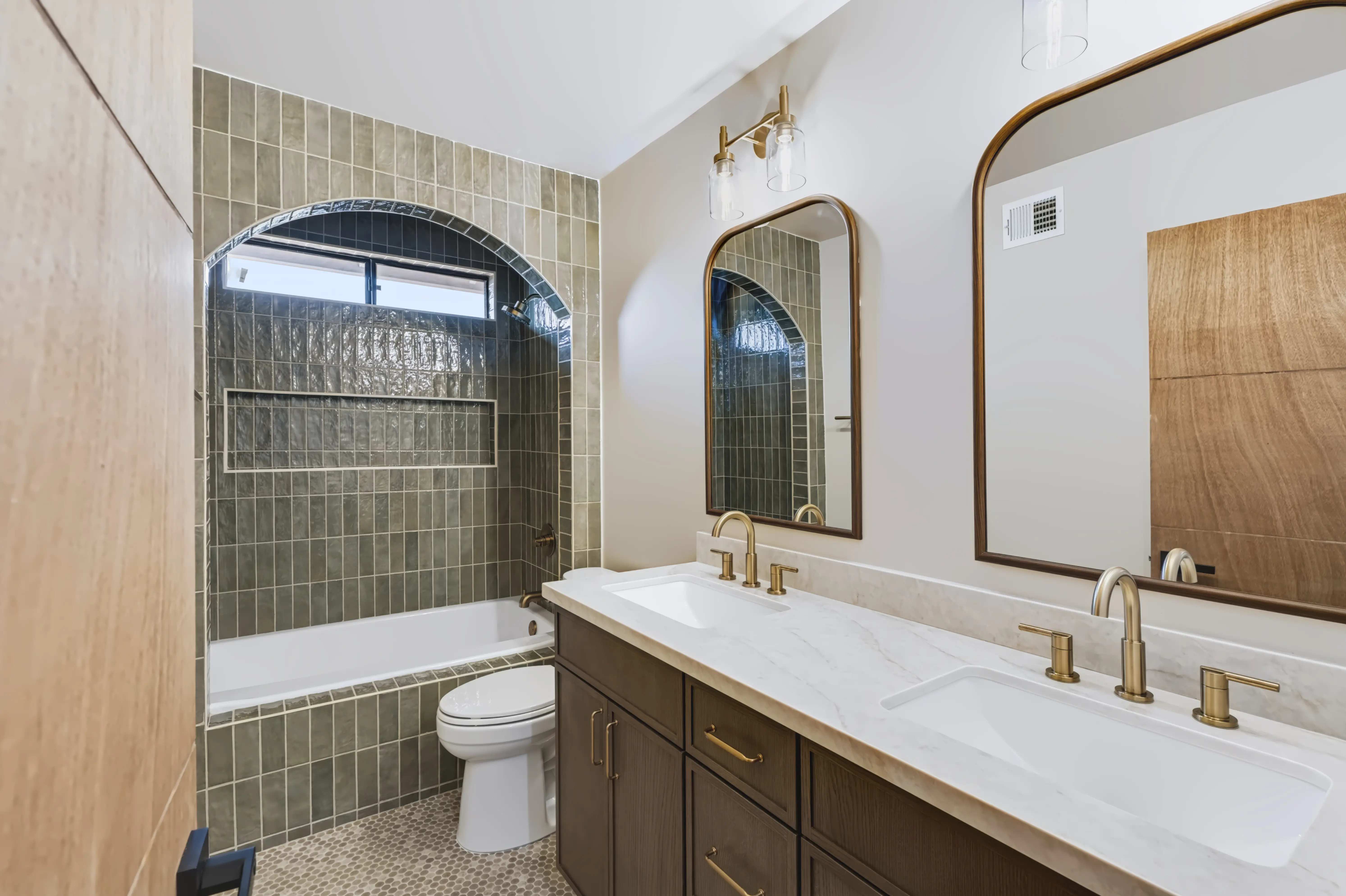 Guest bath with a green zellige-tile arch framing the tub and walnut-framed mirrors over a marble vanity