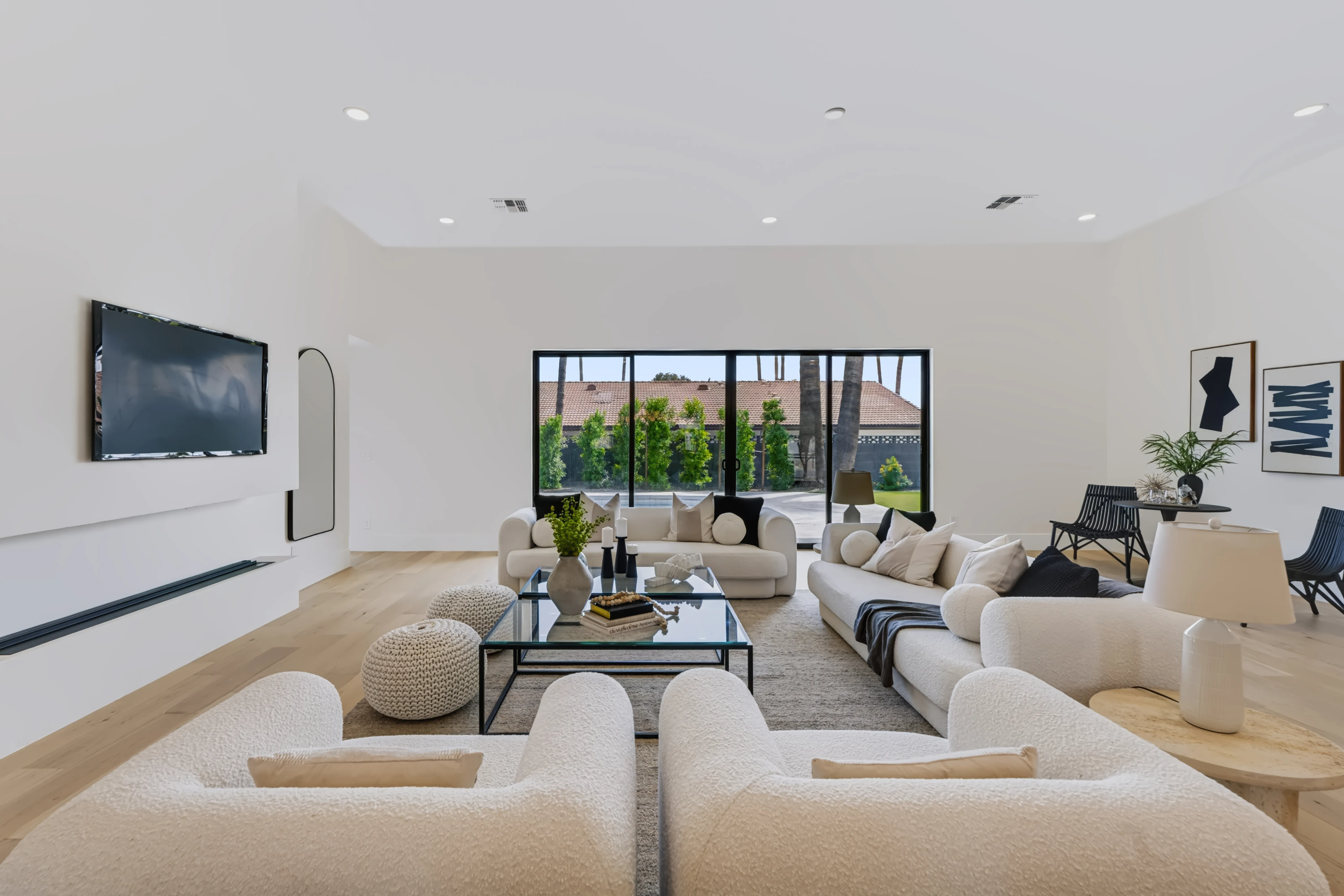 Great room from the far end, a black framed window wall onto the clipped hedge and palms with white oak floors throughout
