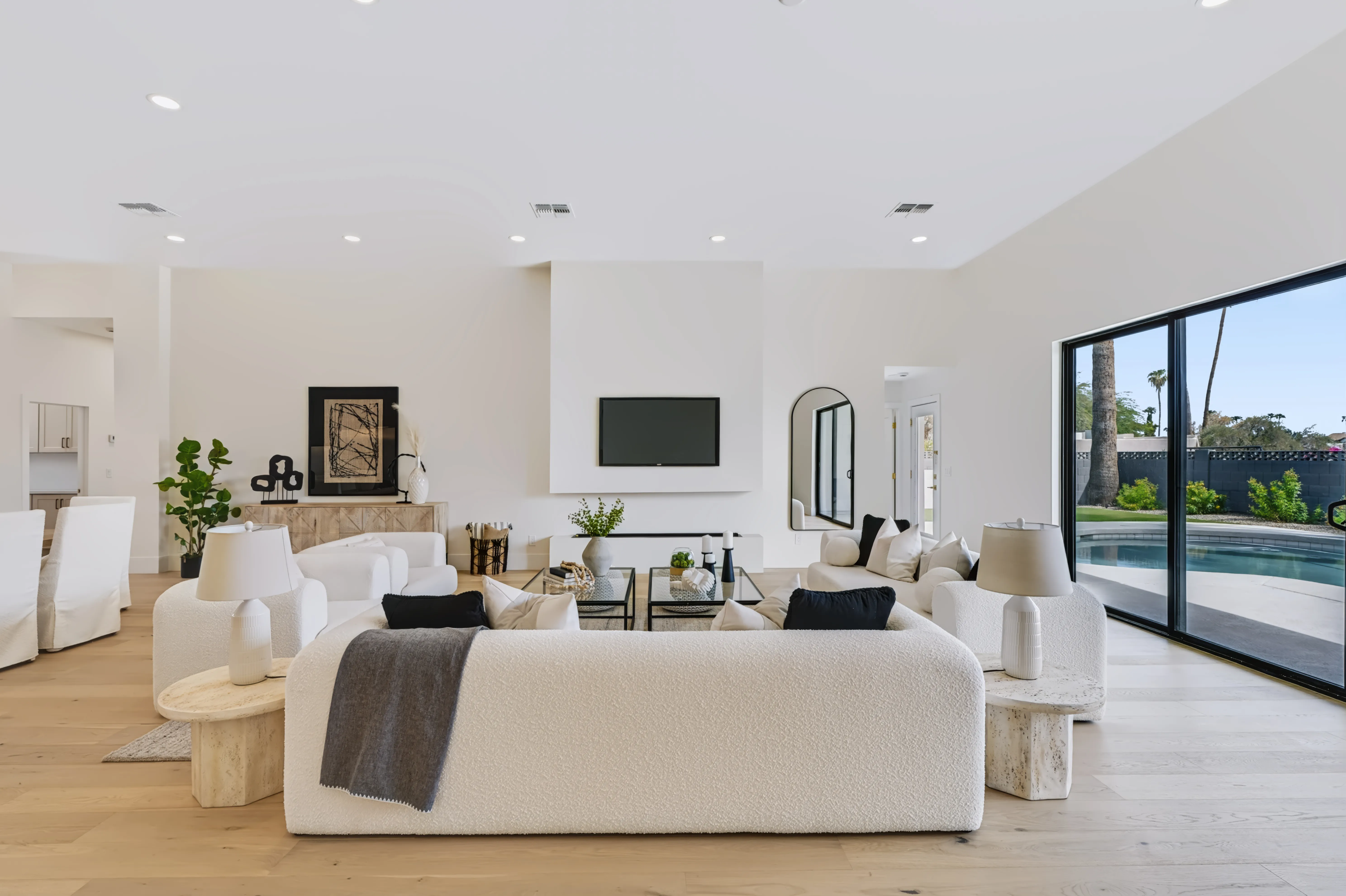 Living room under a raised ceiling, an arched mirror beside the fireplace and a sliding glass wall onto the pool deck
