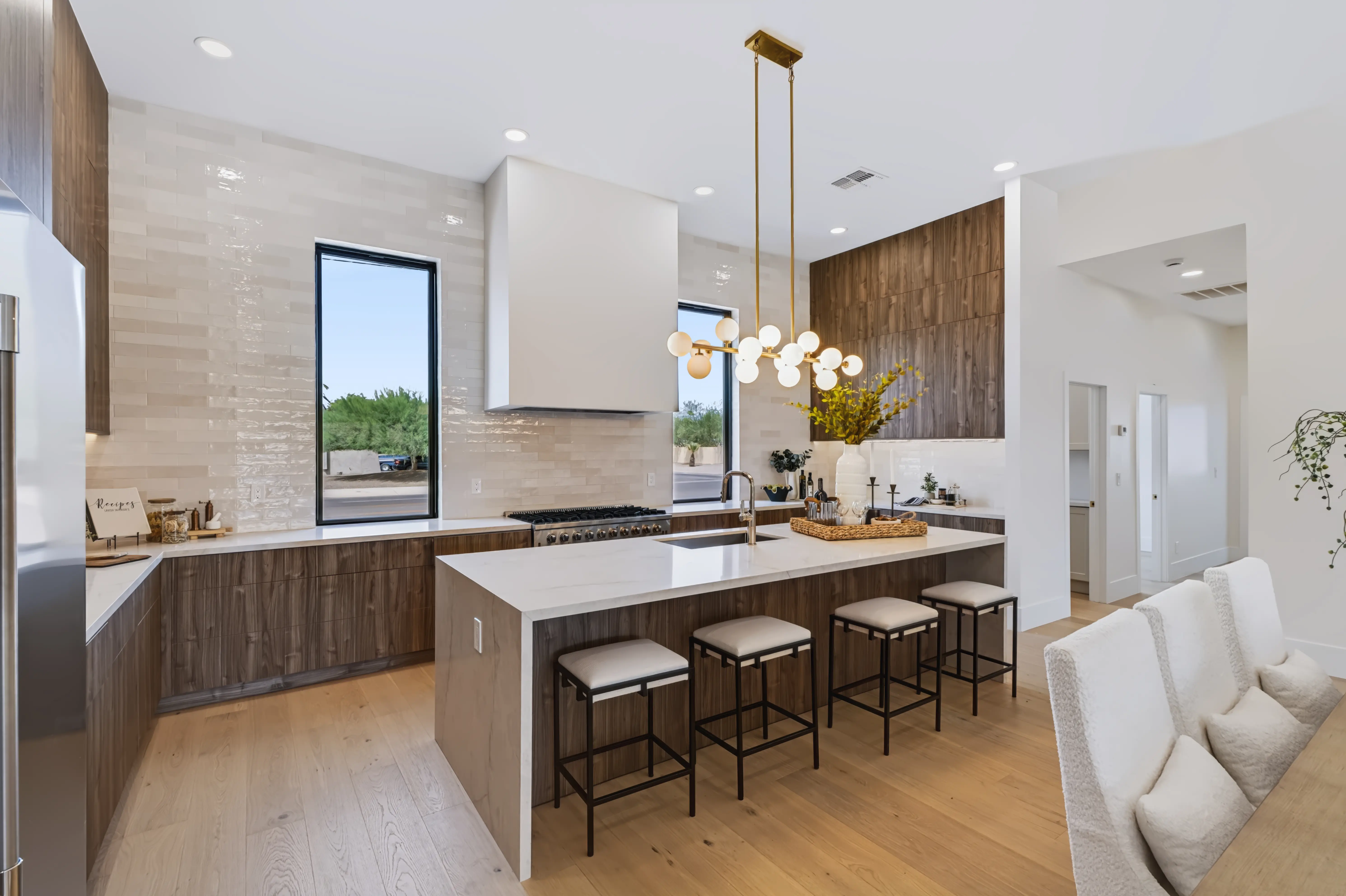 Kitchen with a marble waterfall island and four leather stools, a white plaster hood between walnut cabinetry and a brass globe chandelier