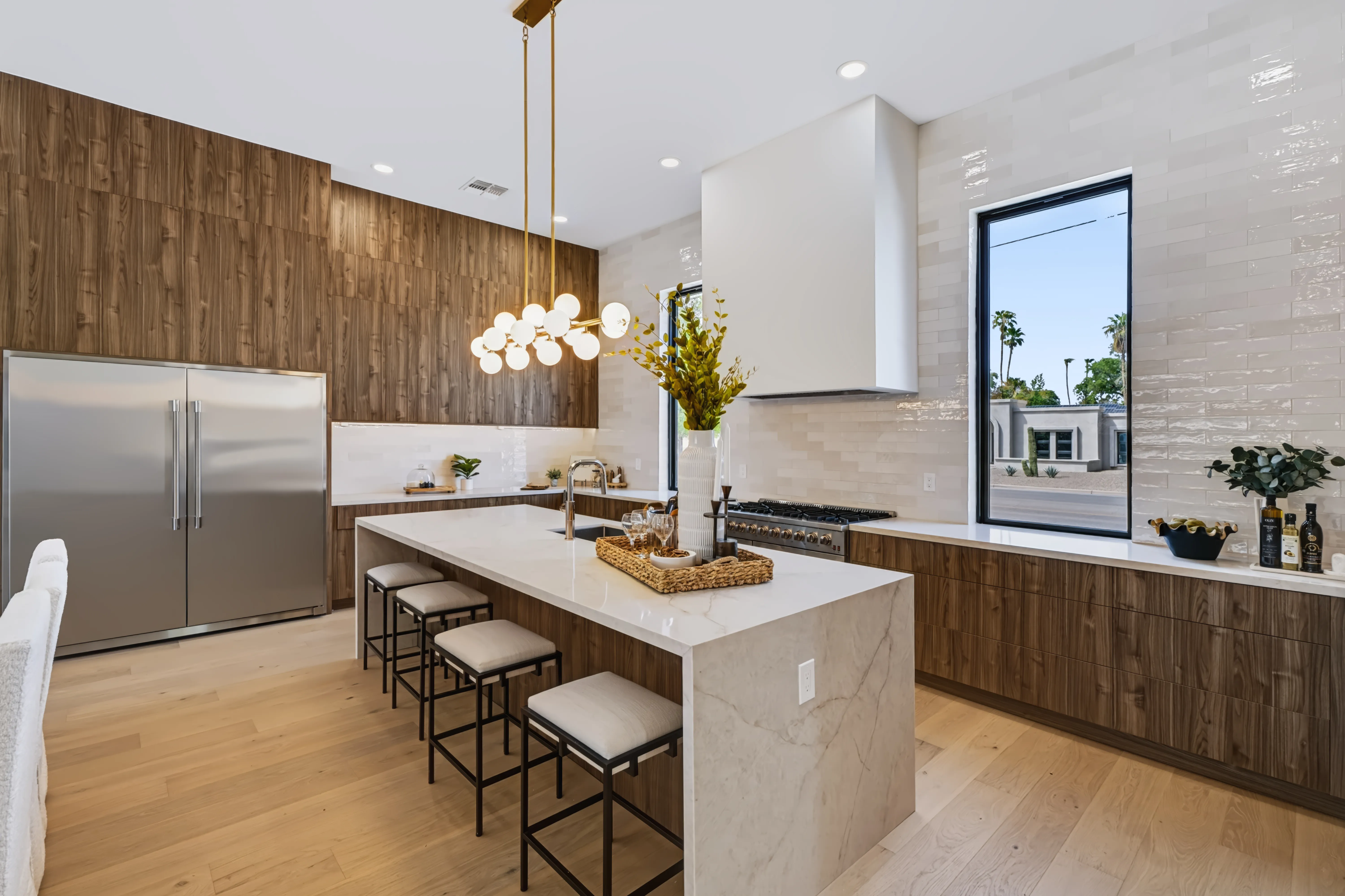 Kitchen from the dining end, walnut slat wall and full height fridge beside the range under a stacked tile backsplash