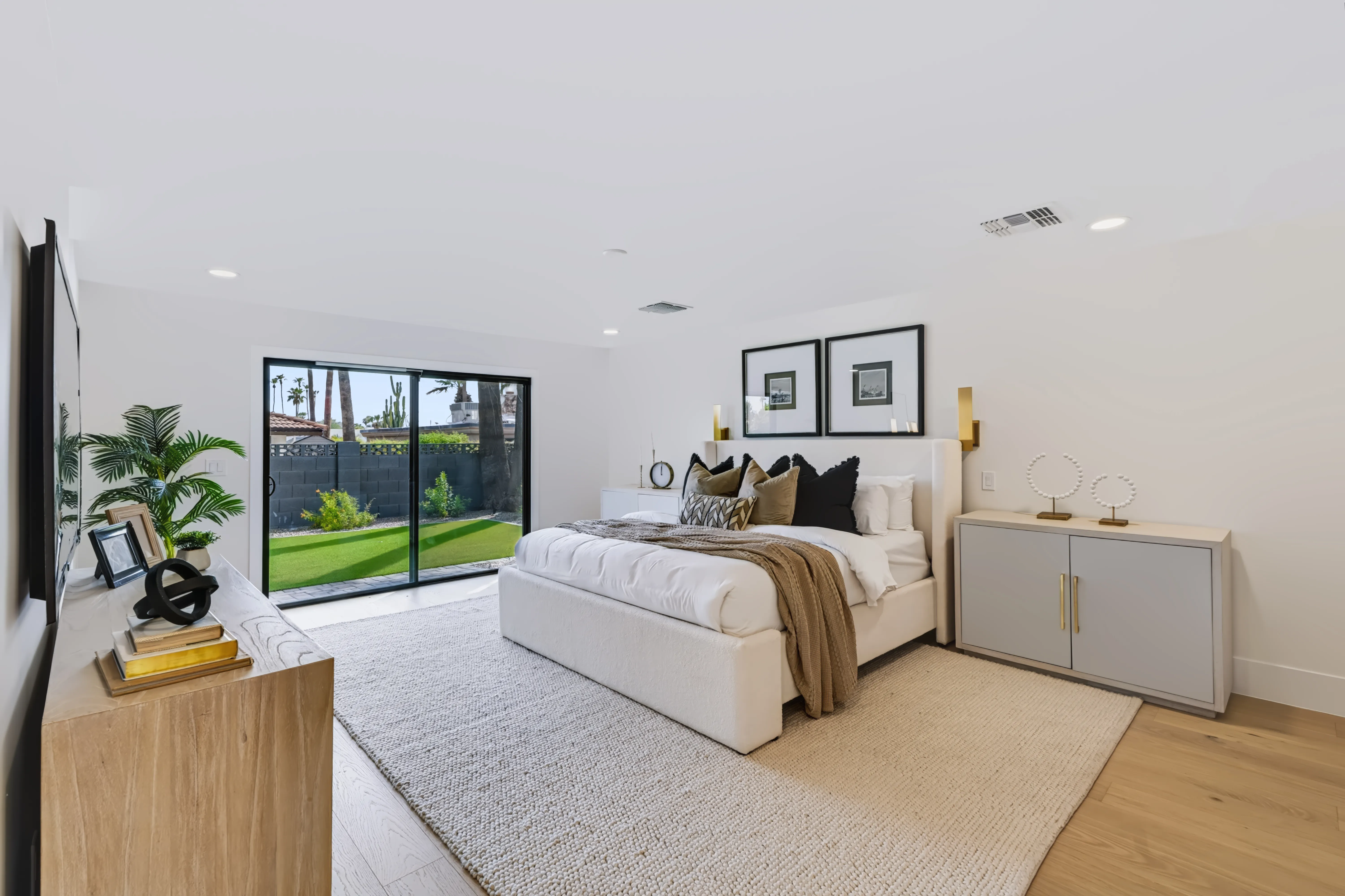 Primary bedroom with an upholstered bed between brass sconces and a sliding glass wall onto the turf lawn