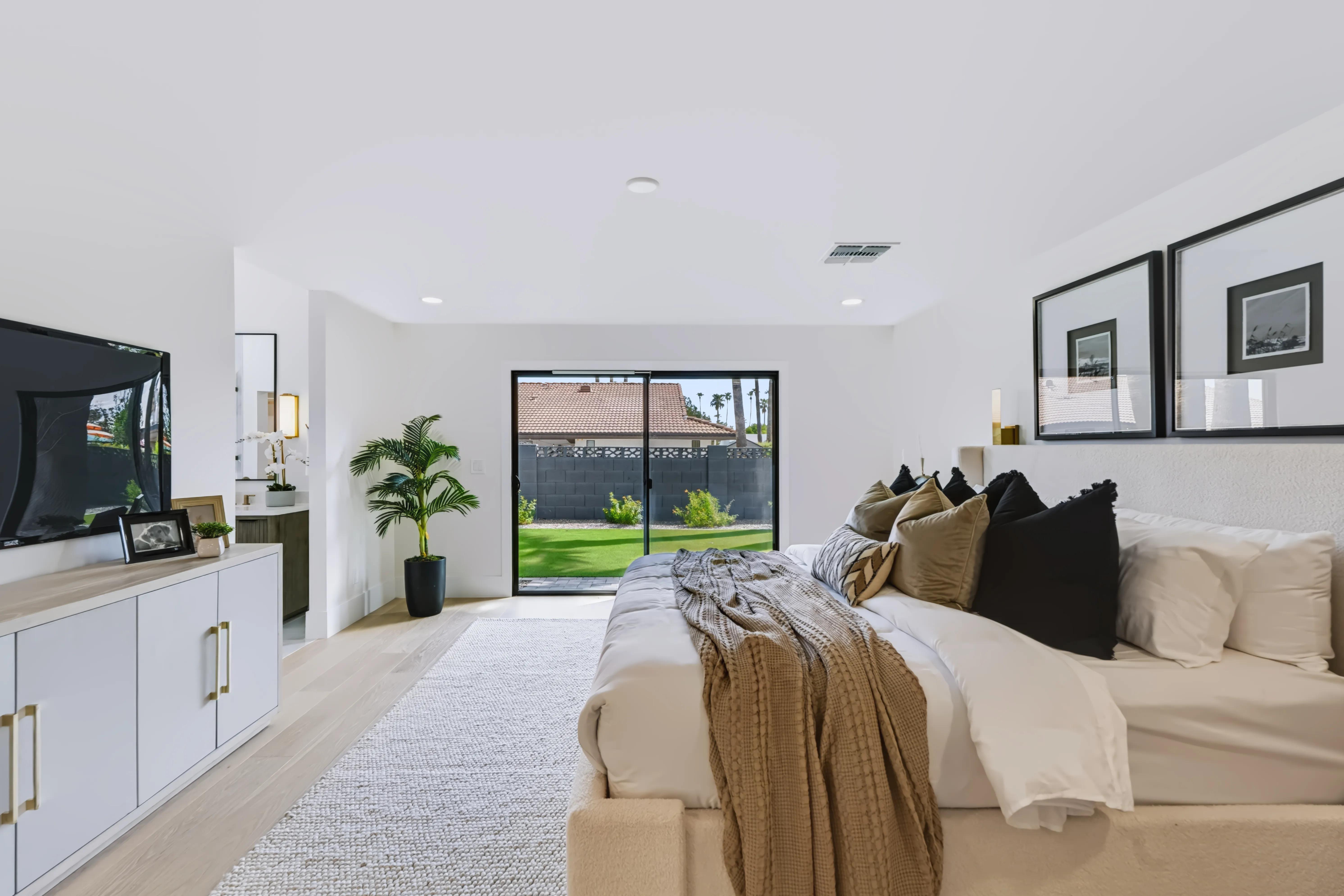 Primary bedroom from the foot of the bed, a low console and potted palm beside the slider onto the garden