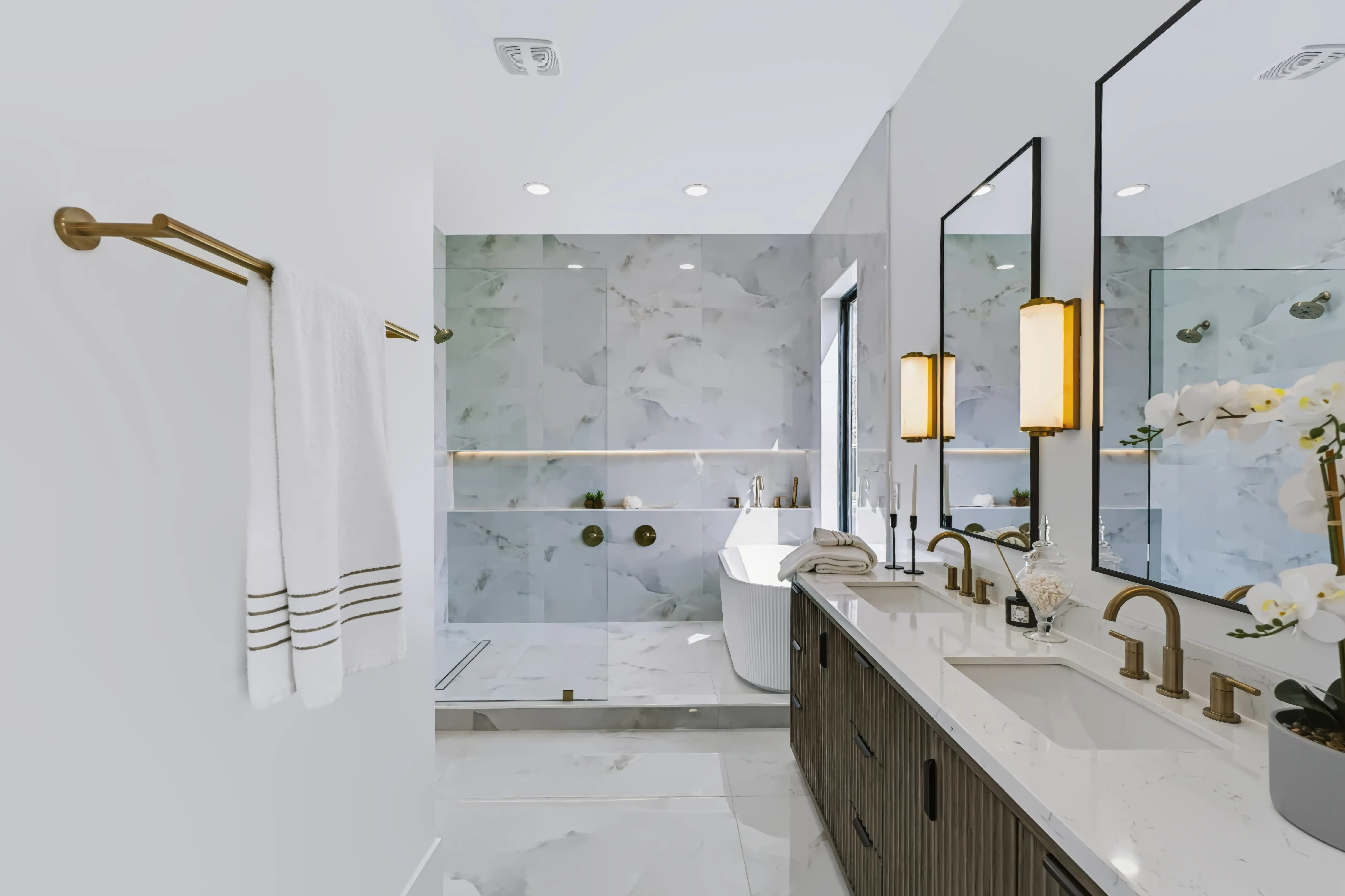 Primary bath along the fluted walnut double vanity, brass fittings and black framed mirrors under lit sconces