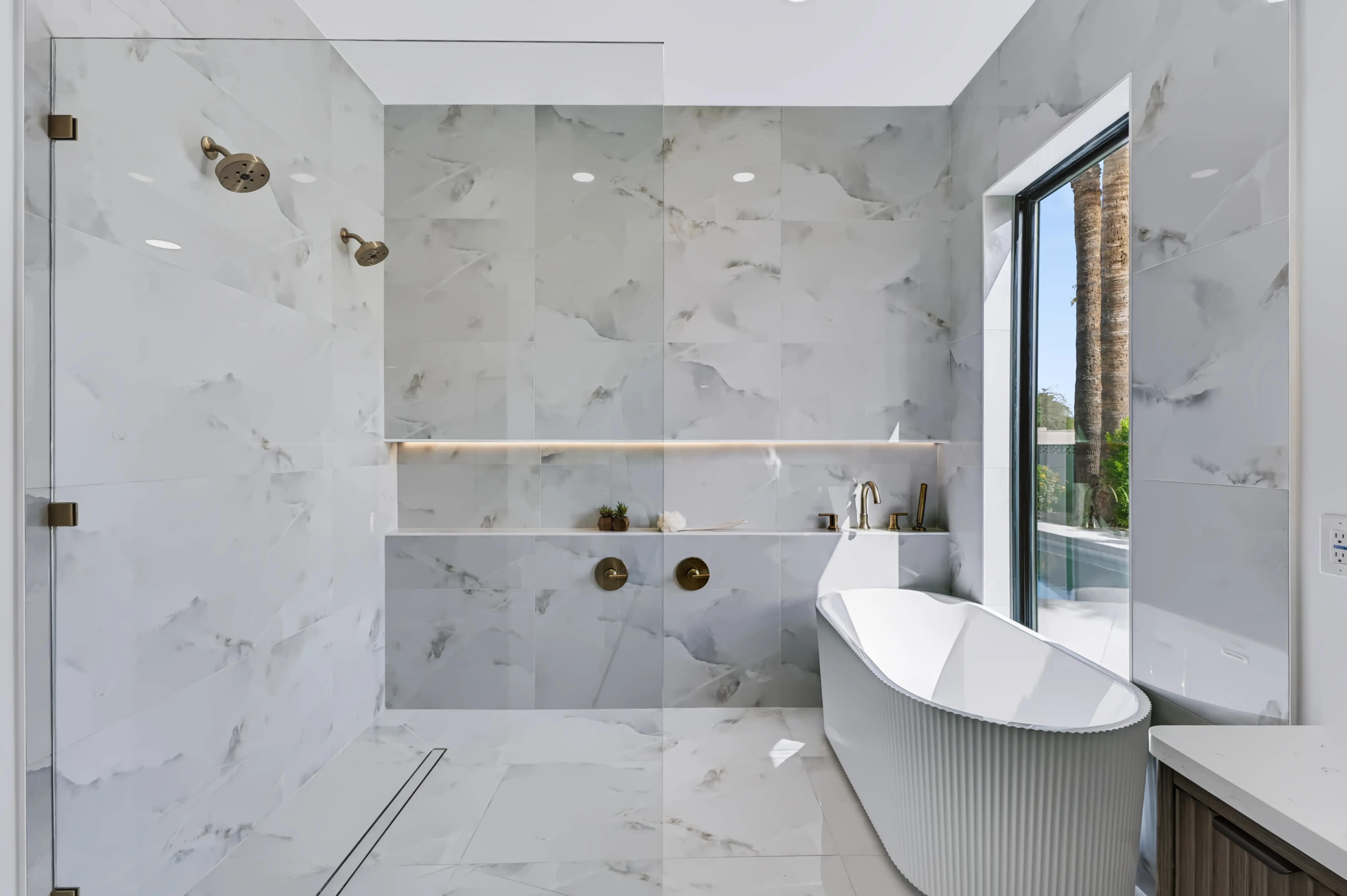 Marble wet room with a walk in shower, a lit niche running the wall and a fluted freestanding tub beneath the window