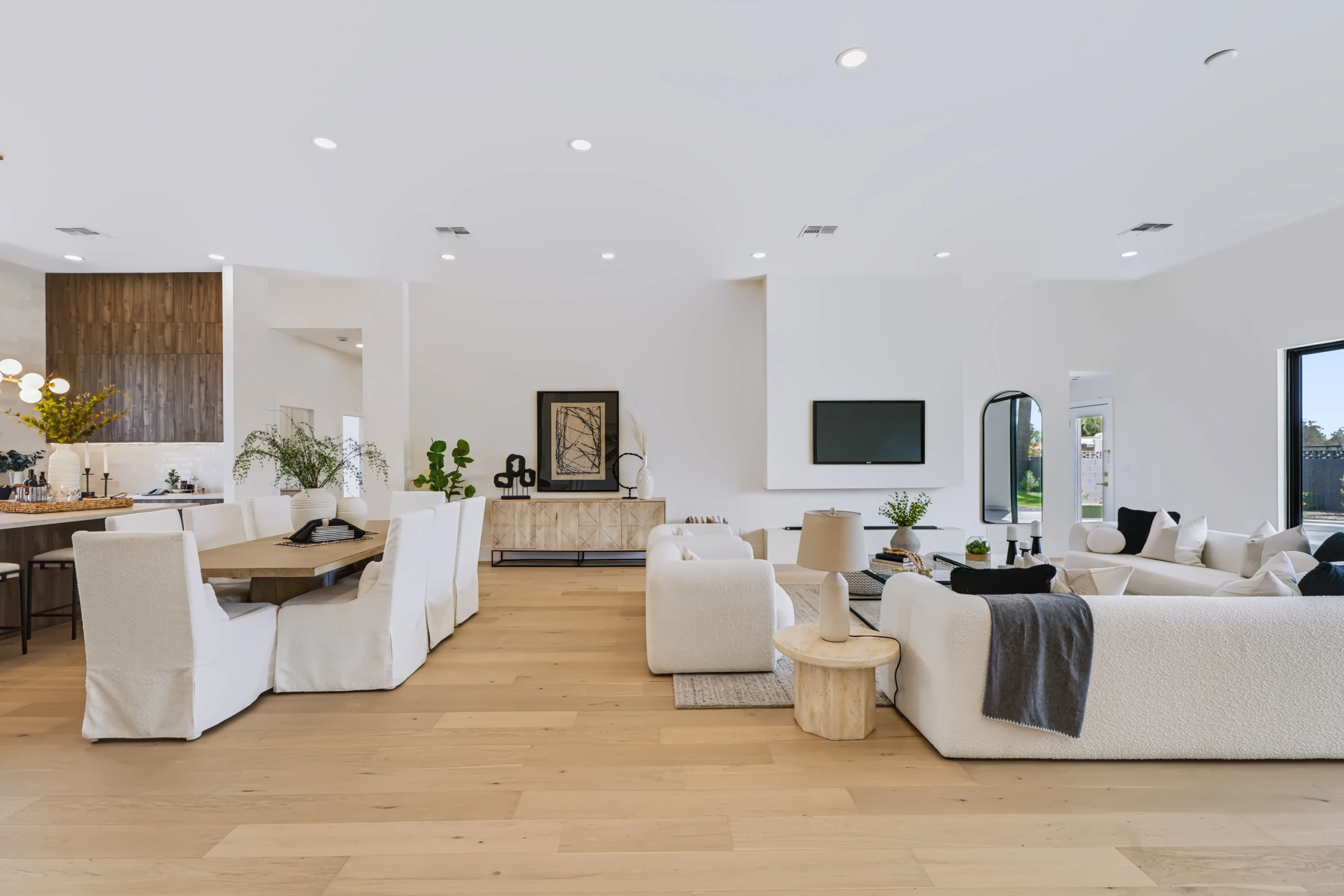 Open plan from the hall, the dining table and slipcovered chairs in front of the walnut kitchen with the living room beyond