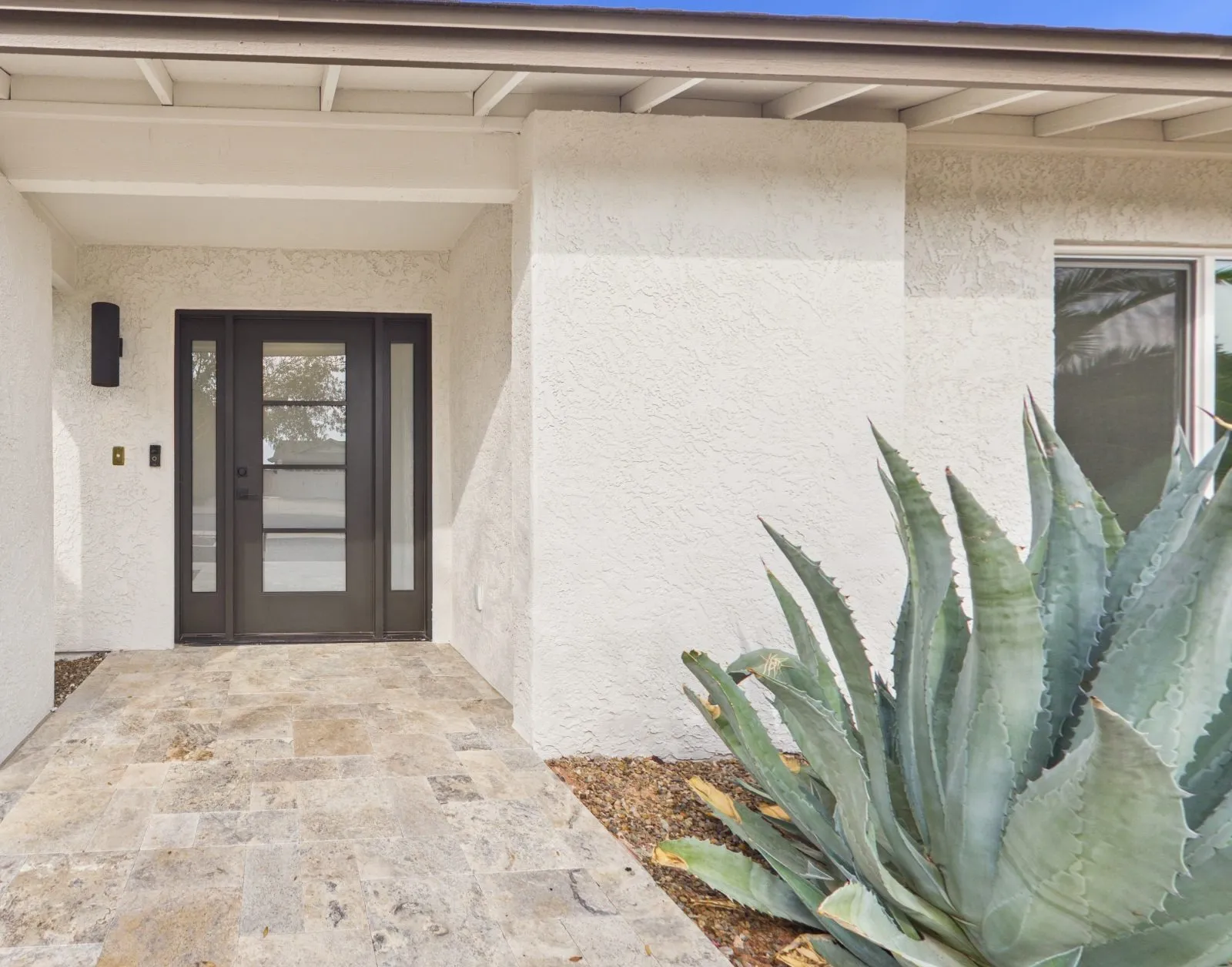 Recessed entry with a glass-panel front door and sidelights, a travertine walk and a blue agave against textured white stucco