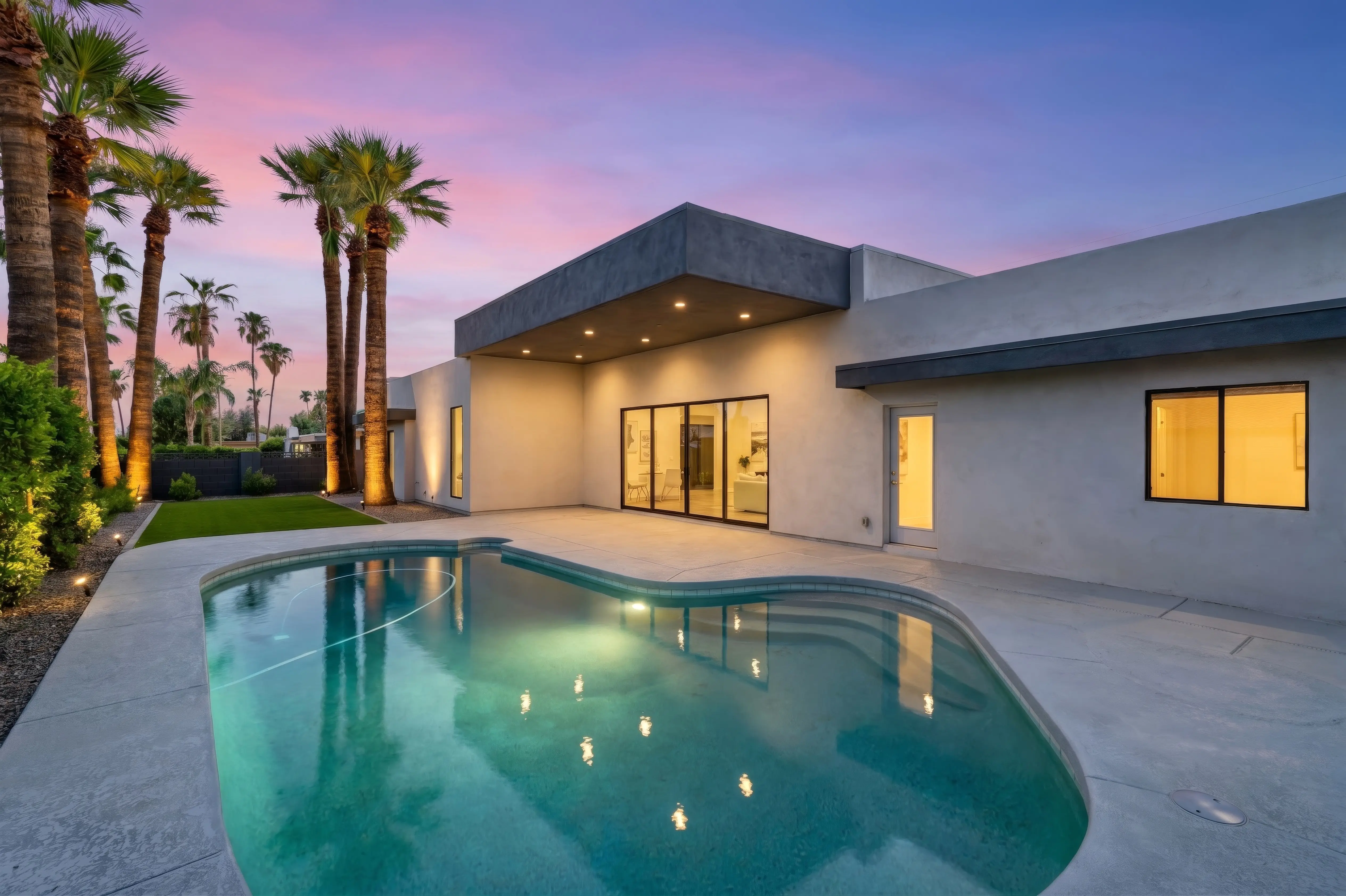 Phoenix backyard at twilight, the pool lit from within and the covered patio downlights on beneath a pink and violet sky