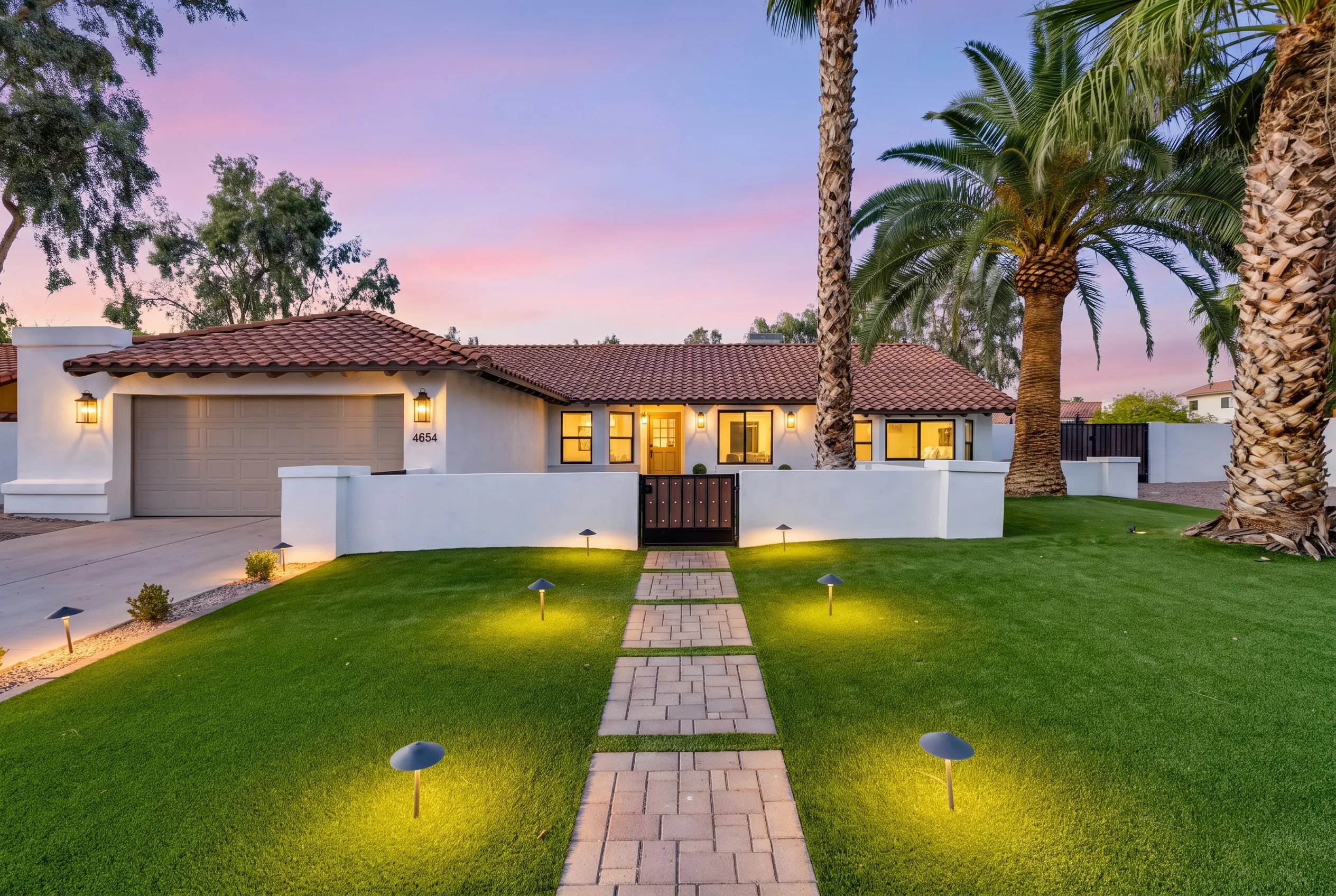 A single-story Scottsdale home at twilight, its windows glowing and a lit paver walk crossing the lawn